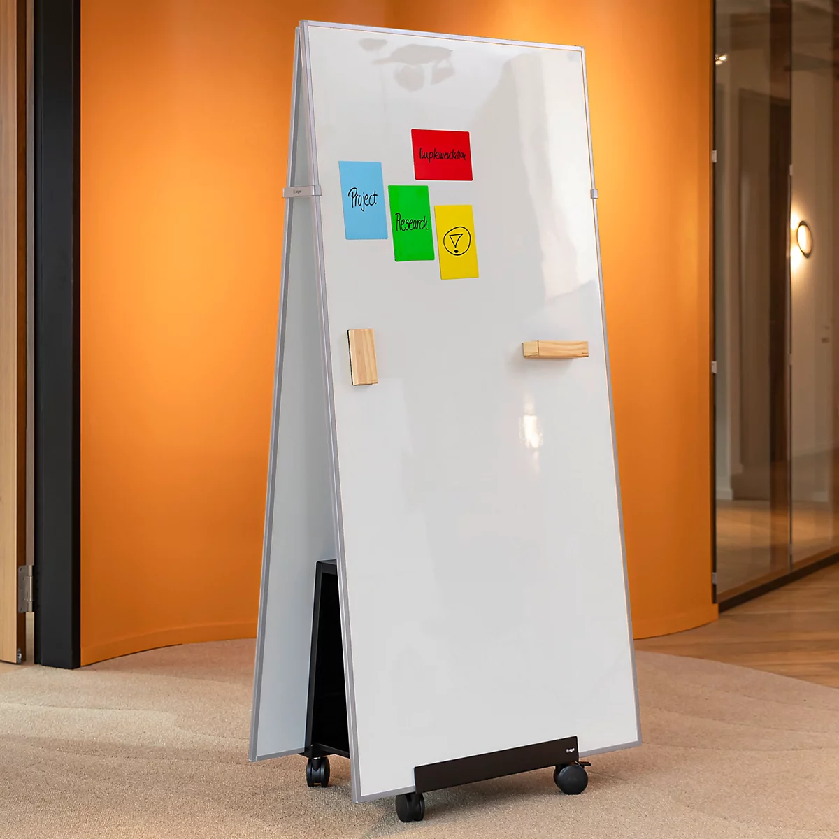 Mobiles Whiteboard auf Rollen mit bunten Haftnotizen in einem modern eingerichteten Büro.