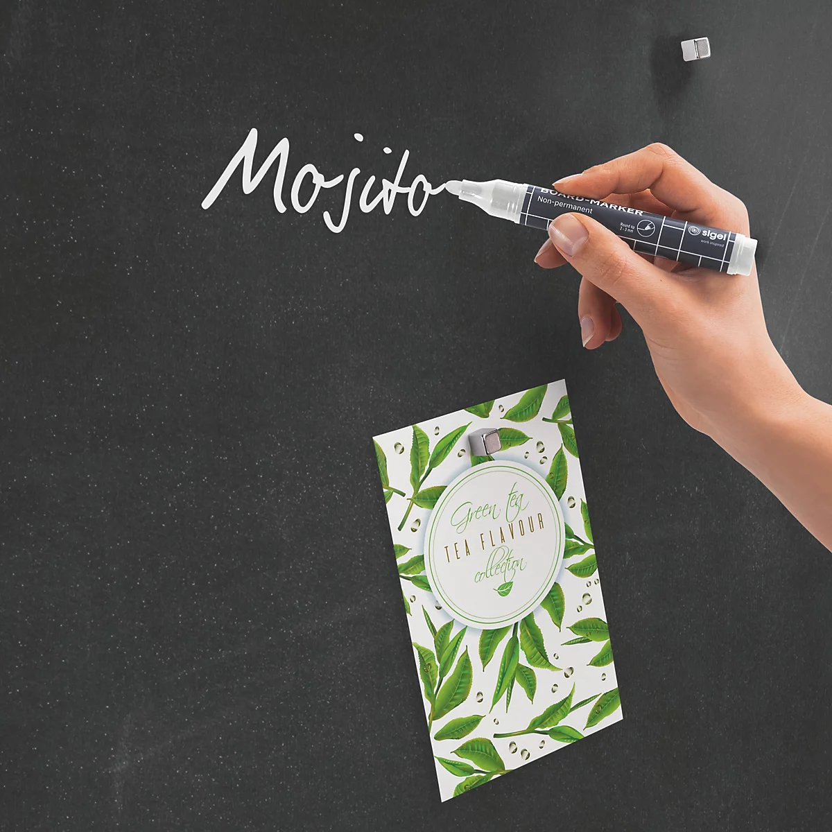 Hand schreibt Mojito mit weißem Stift auf einer schwarzen Tafel. Darunter eine Karte mit grünen Blättern.