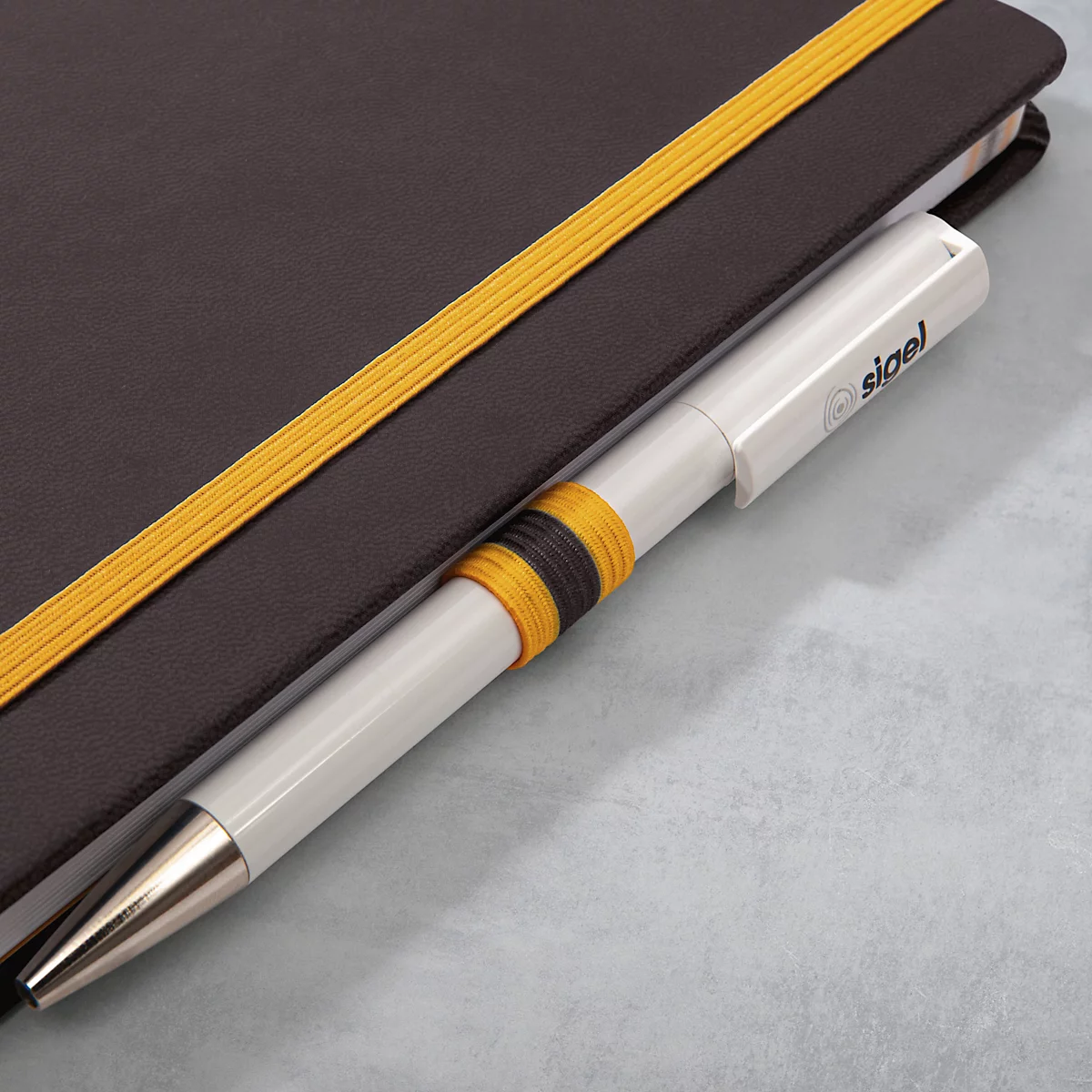 Hellgrauer Stift steckt in Notizbuch. Buch ist braun, hat gelbes Gummiband. Stift hat gelb-schwarze Ringe.