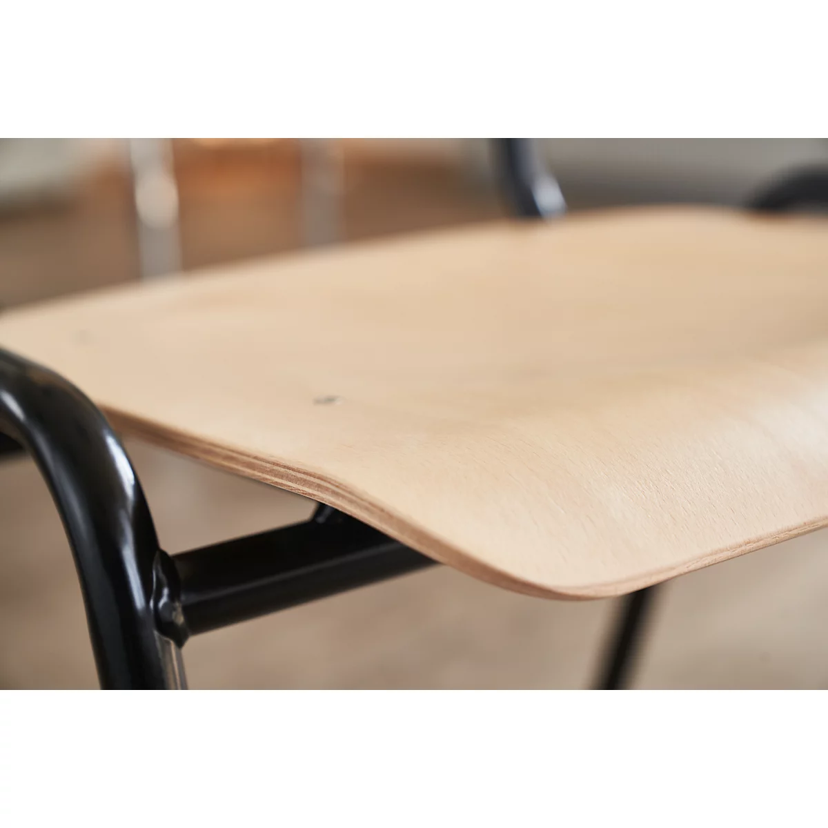 Primer plano de una silla con superficie de madera clara y marco de metal negro.