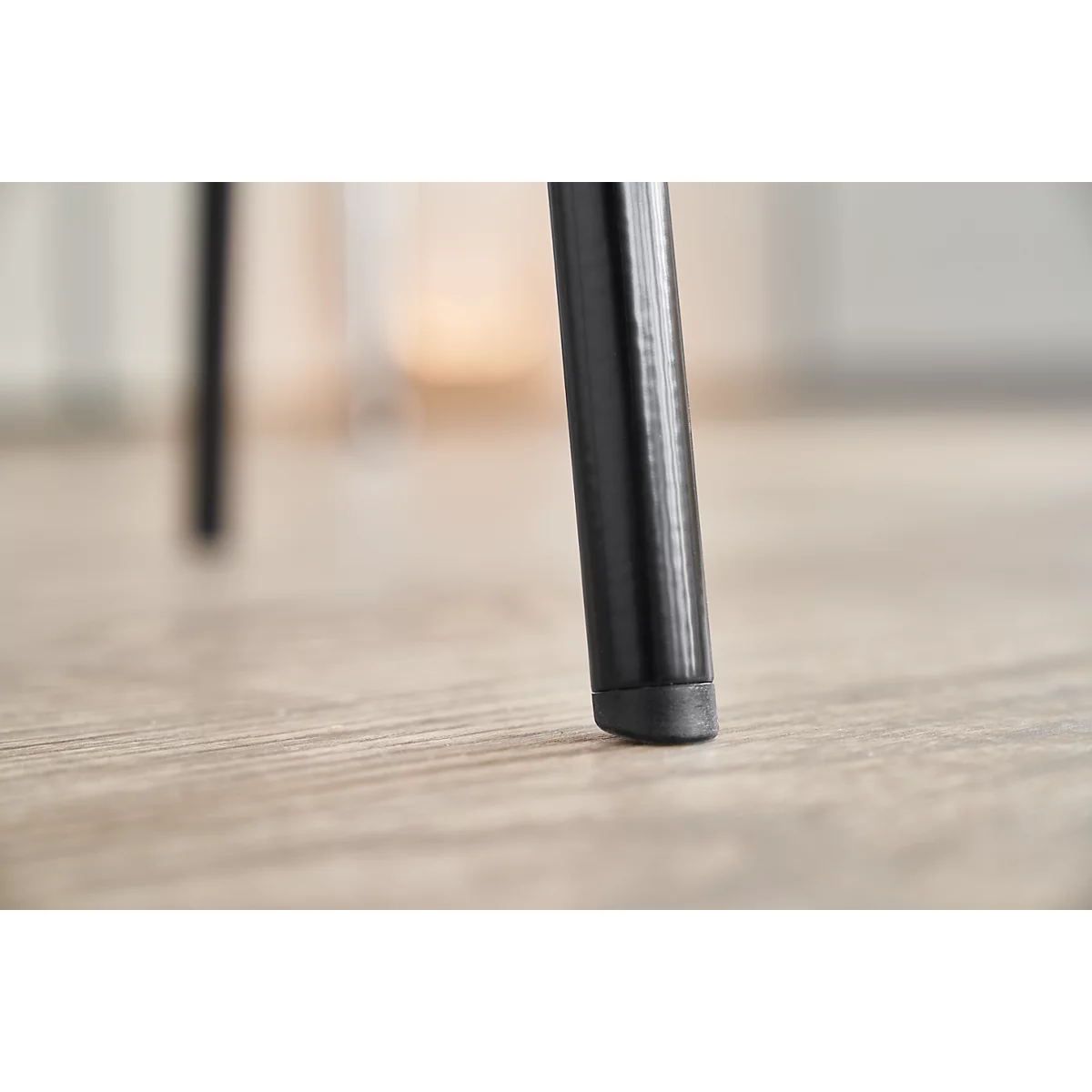 Primer plano de una pata de silla negra sobre un suelo de madera. La atención se centra en la parte inferior de la pata.