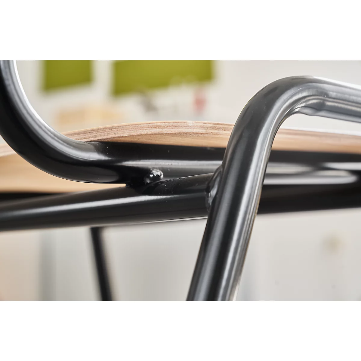 Primer plano de una silla. Estructura de metal negro, asiento de madera clara.