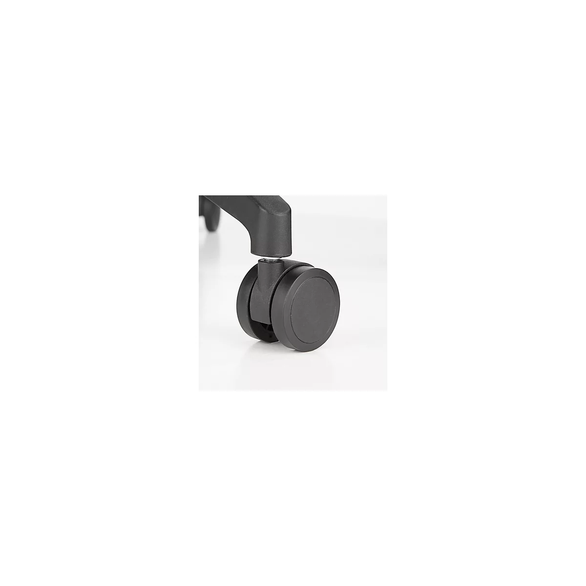 Primer plano de una rueda de silla de oficina negra. La rueda se apoya sobre una superficie blanca.