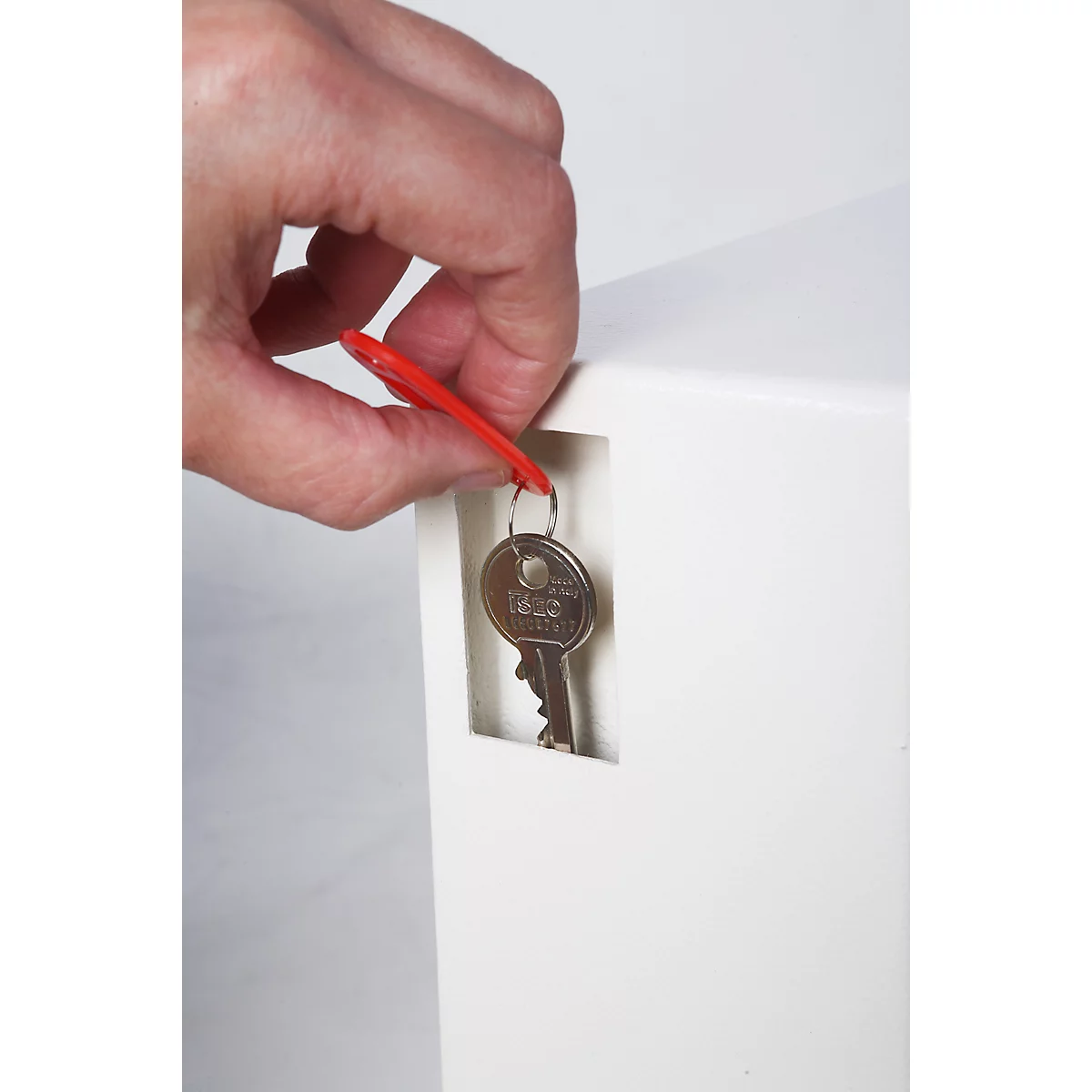 Een hand met een rode tag en een sleutel voor een witte kast.