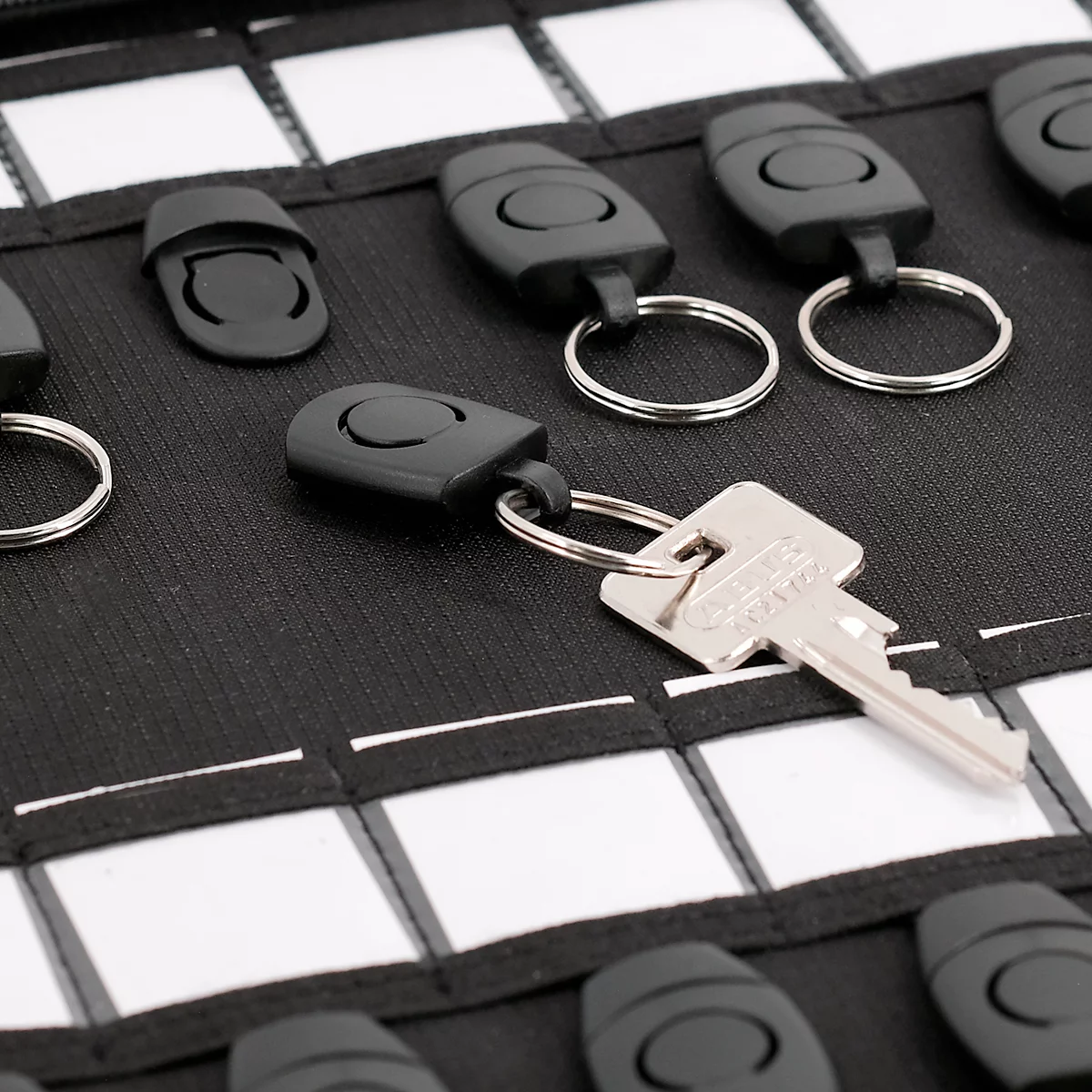 Close-up van een sleutelorganizer met sleutels en sleutelhangers op zwarte stof met witte vierkanten. Eén sleutel valt op.