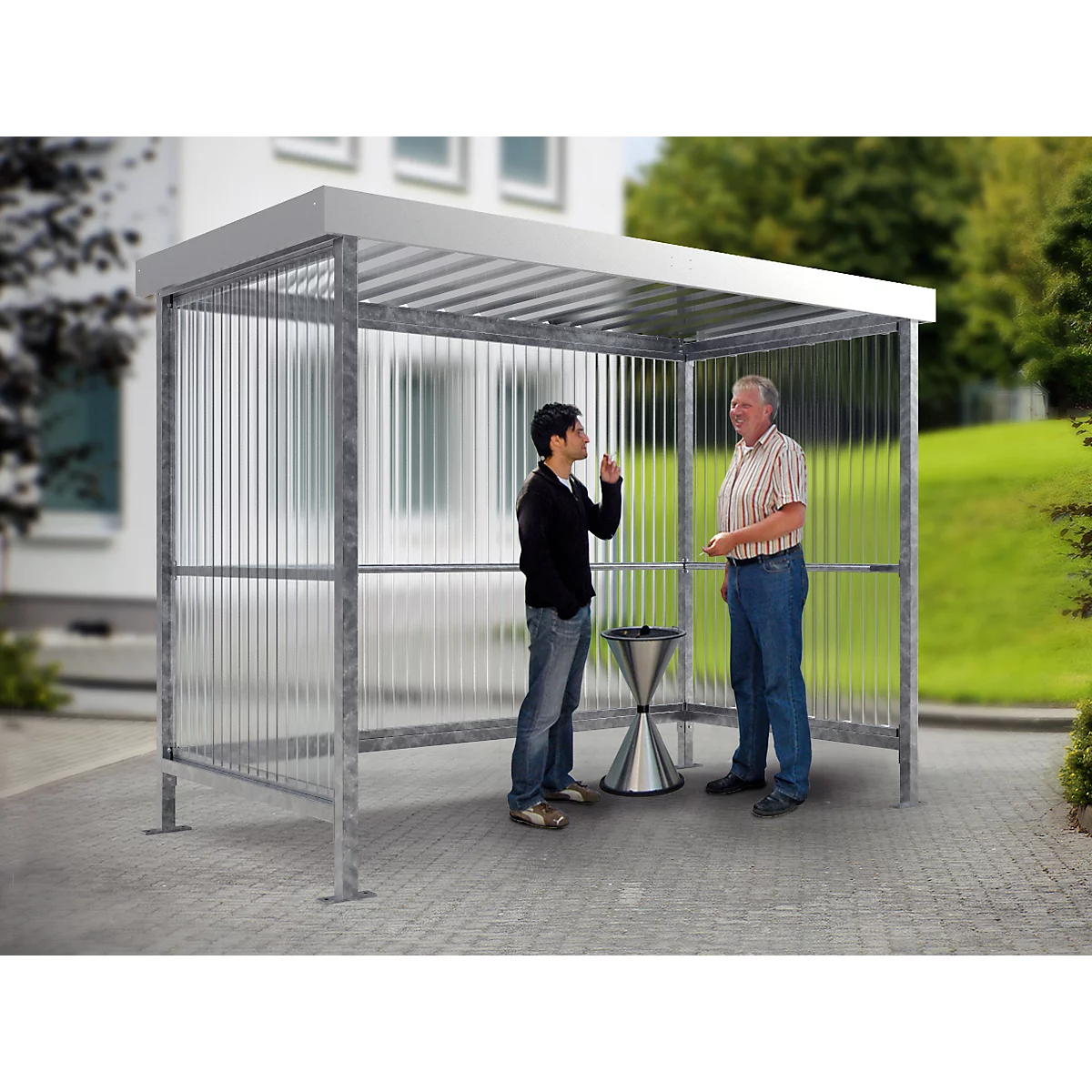 Two men stand under a shelter. One man points upwards, they seem to be talking to each other.