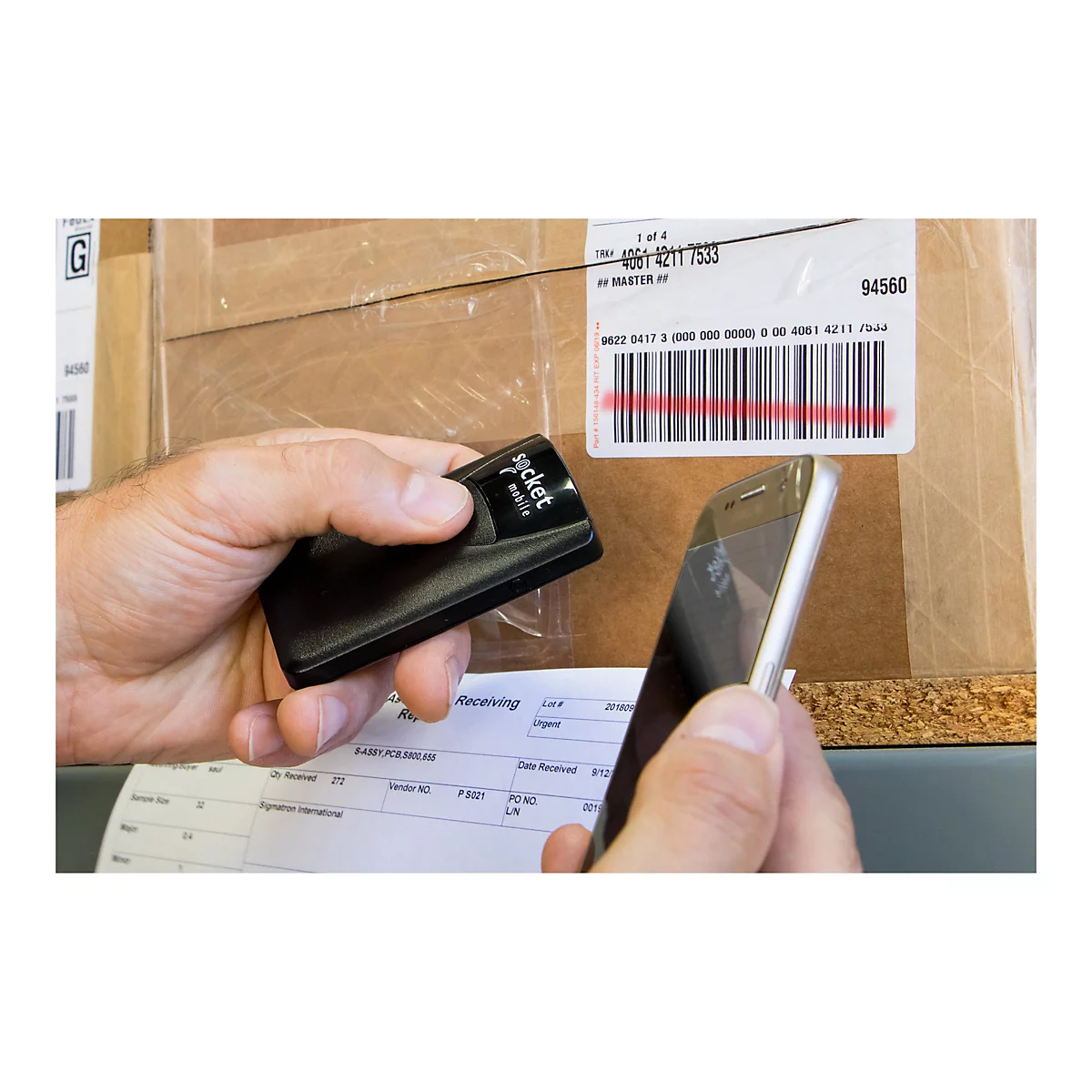 Person scannt Barcode auf Karton mit einem Smartphone und einem schwarzen Socket Mobile-Gerät.