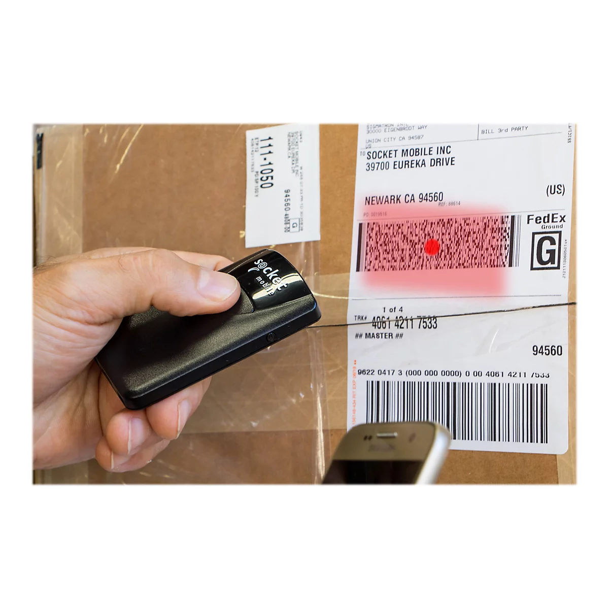 Person scannt Paketaufkleber mit Barcode-Scanner. Barcode wird rot markiert. Telefon im unteren Bildbereich.