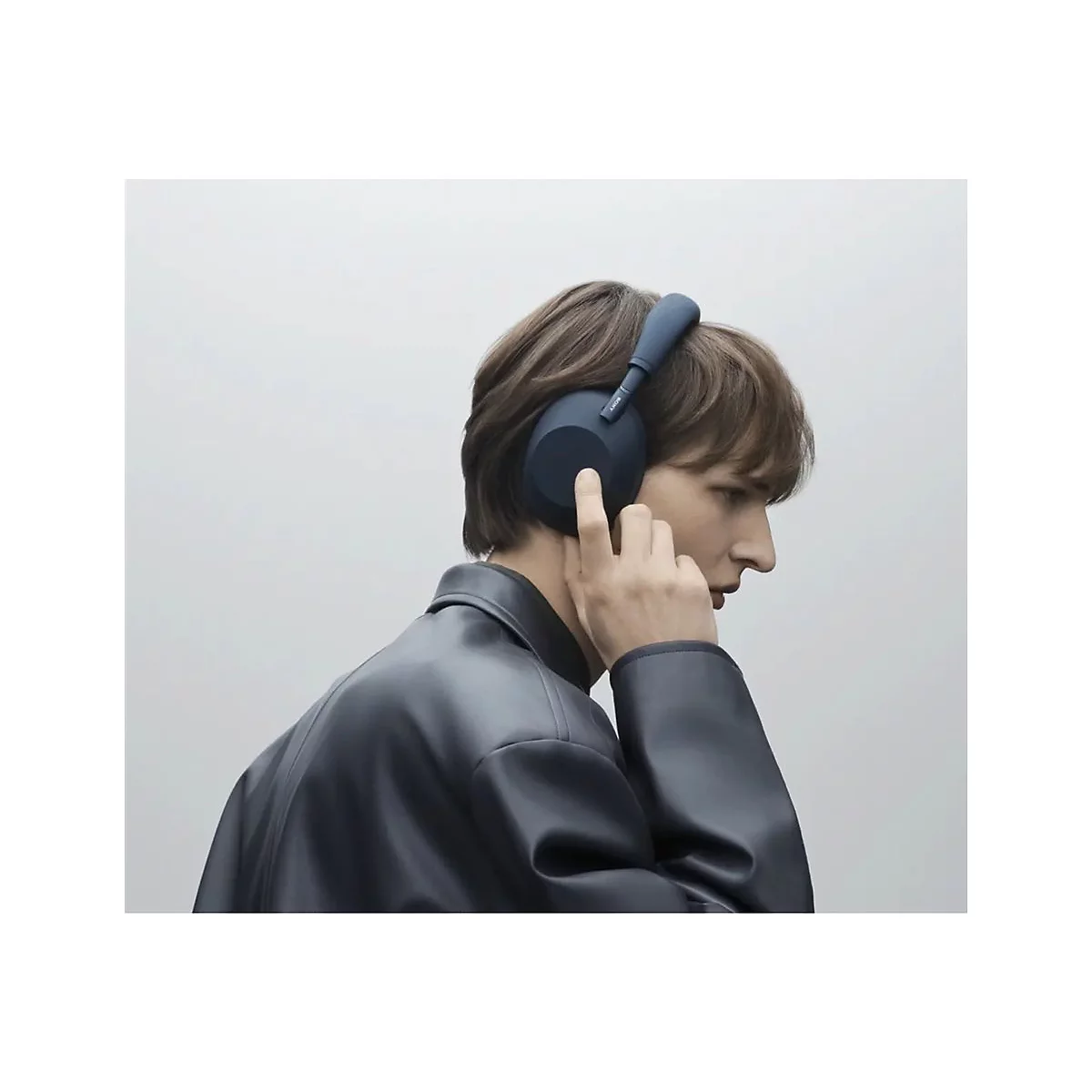 Junger Mann mit blauen Kopfhörern. Er berührt das Headset, während er zur Seite schaut.