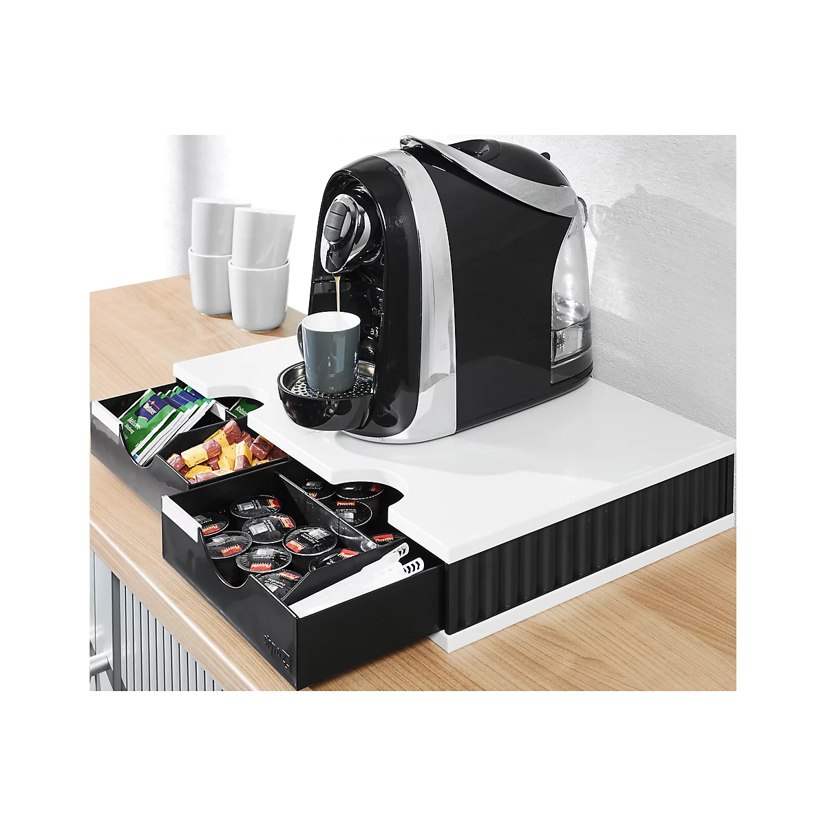 Coffee machine in action, black design, cup filling. Drawers with capsules and snacks. White shelf, wooden table.