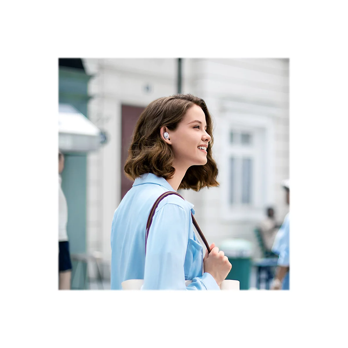 Eine Frau trägt Kopfhörer und lächelt draußen, Sonnenlicht.