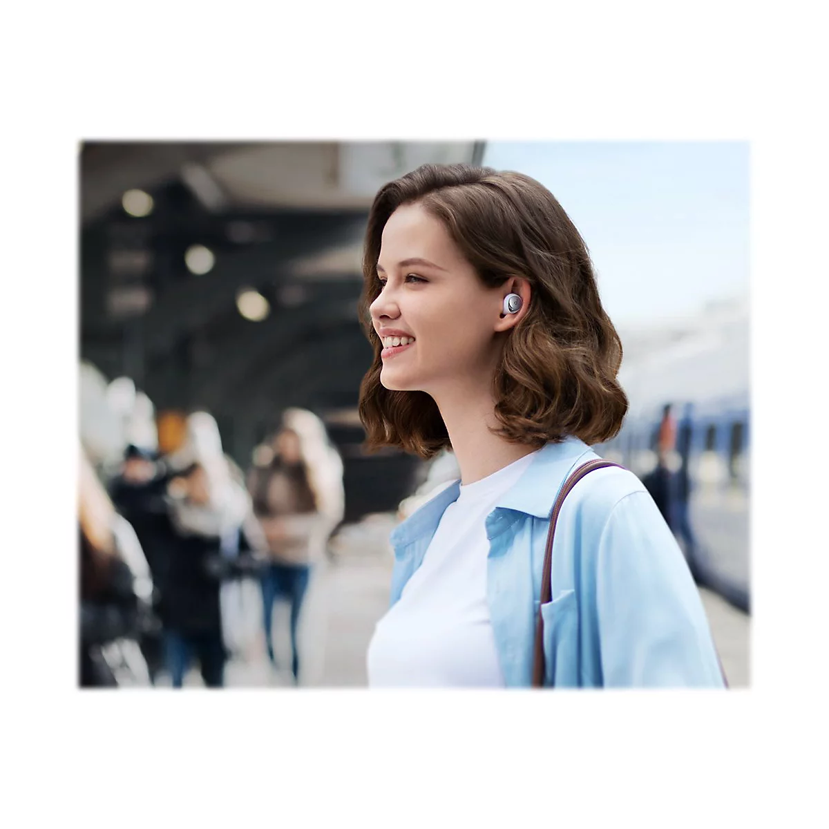 Junge Frau lächelt, trägt Ohrhörer, Hintergrund: Bahnhof.