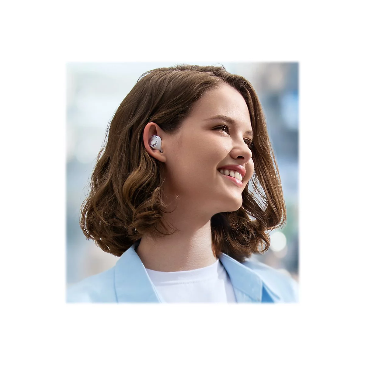 Eine lächelnde Frau mit drahtlosen Ohrhörern. Sie trägt ein hellblaues Jackett.