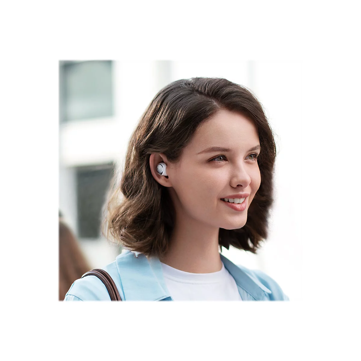 Eine junge Frau mit braunen Haaren und einem Ohrhörer lächelt. Sie trägt eine helle Jacke.