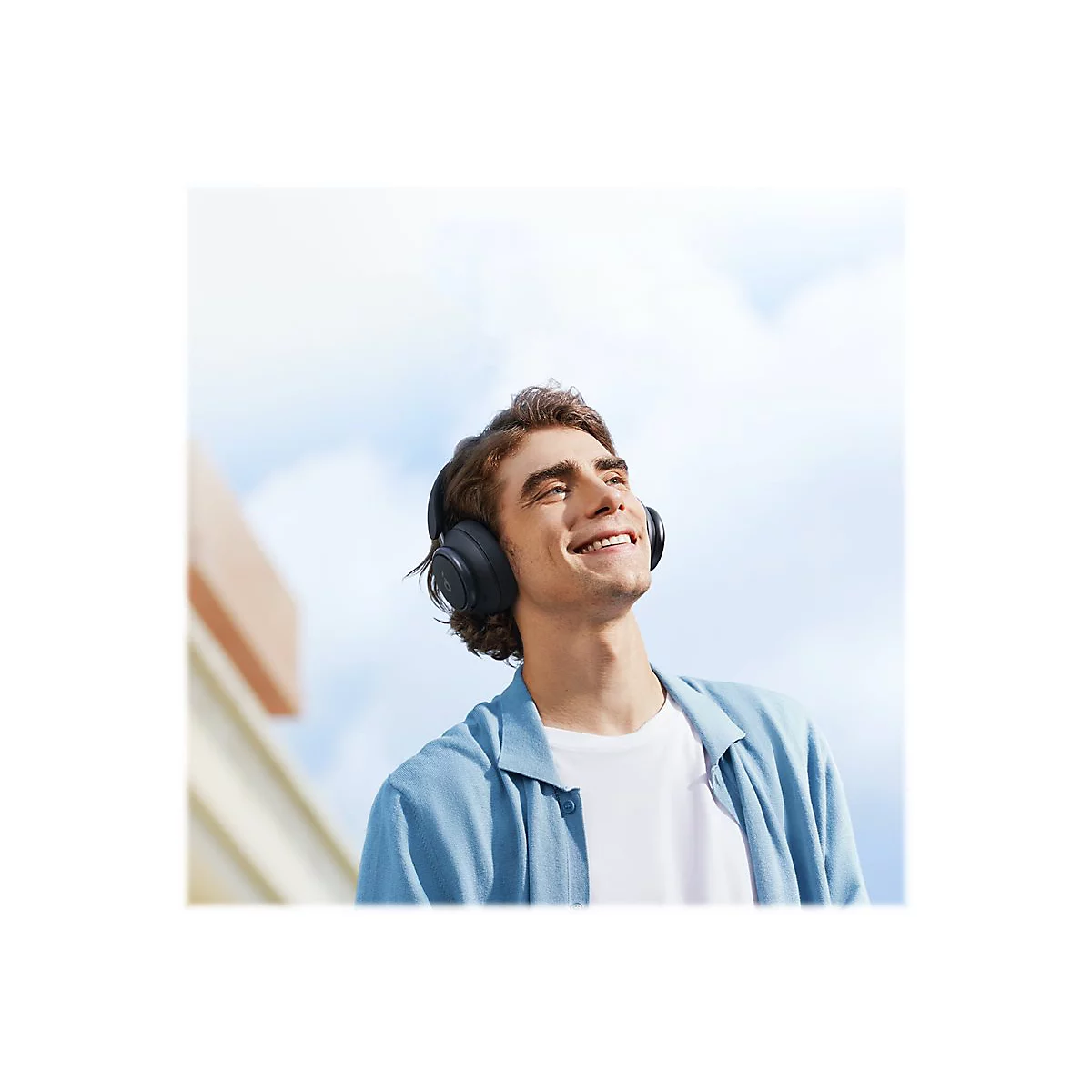 Ein junger Mann mit KopfhÃ¶rern lÃ¤chelt in den Himmel. Er trÃ¤gt ein blaues Hemd und ein weiÃŸes T-Shirt.