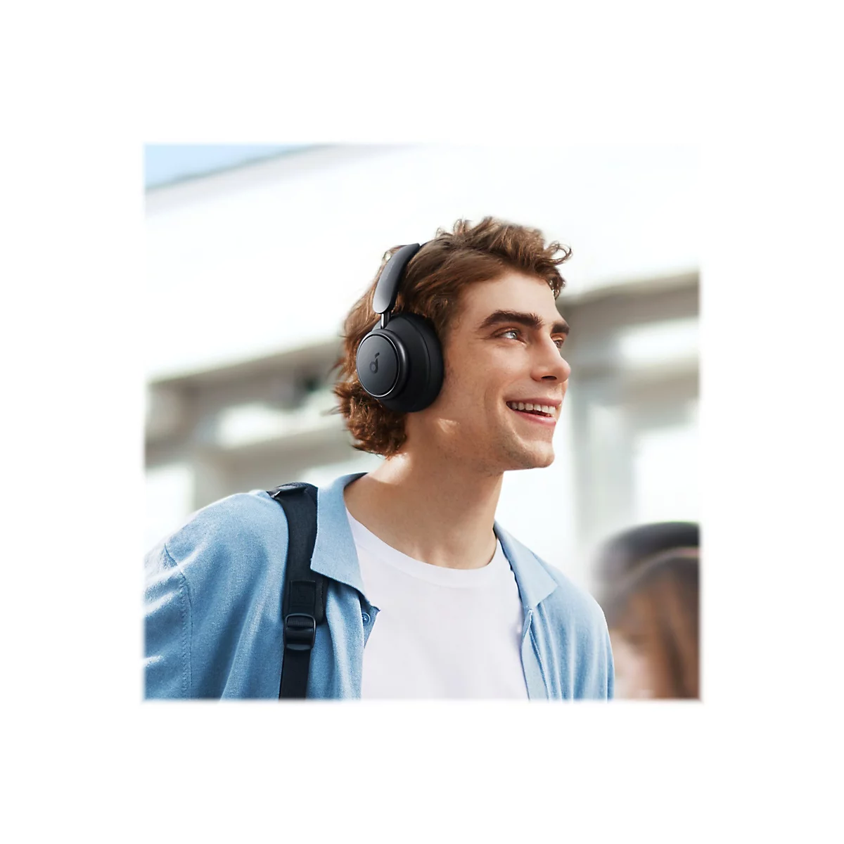 Ein junger Mann mit KopfhÃ¶rern lÃ¤chelt, trÃ¤gt einen Rucksack und blickt nach rechts.