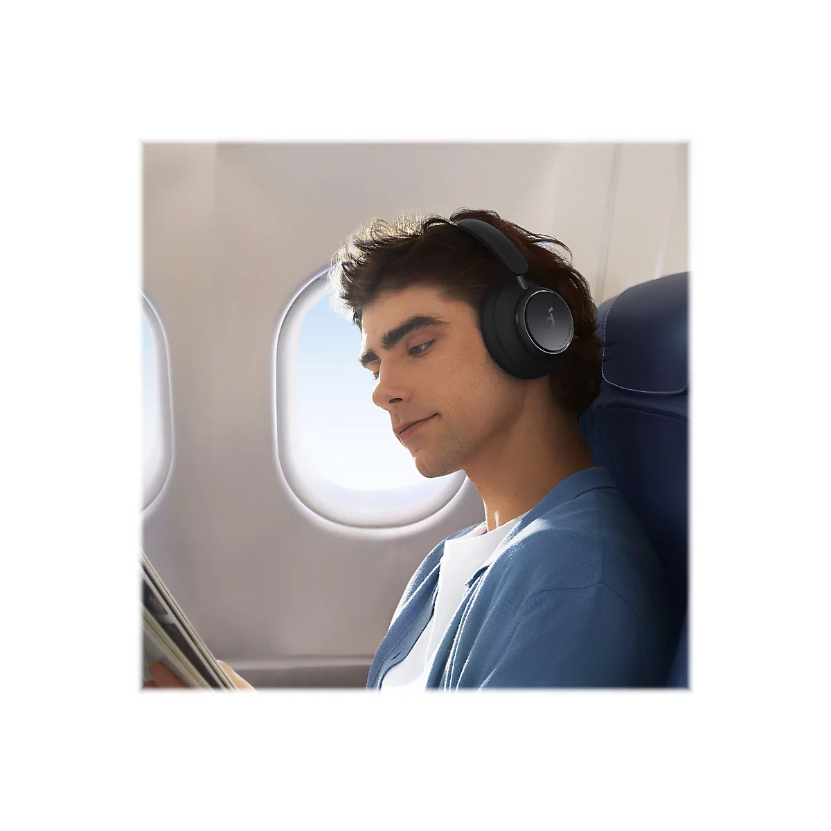 Ein Mann im Flugzeug mit schwarzen KopfhÃ¶rern. Er schaut nach unten auf ein Tablet.