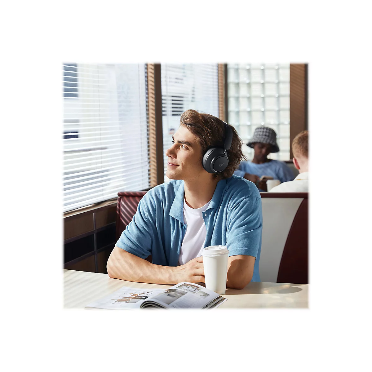 Ein Mann in einem Restaurant, der KopfhÃ¶rer trÃ¤gt und aus dem Fenster schaut.