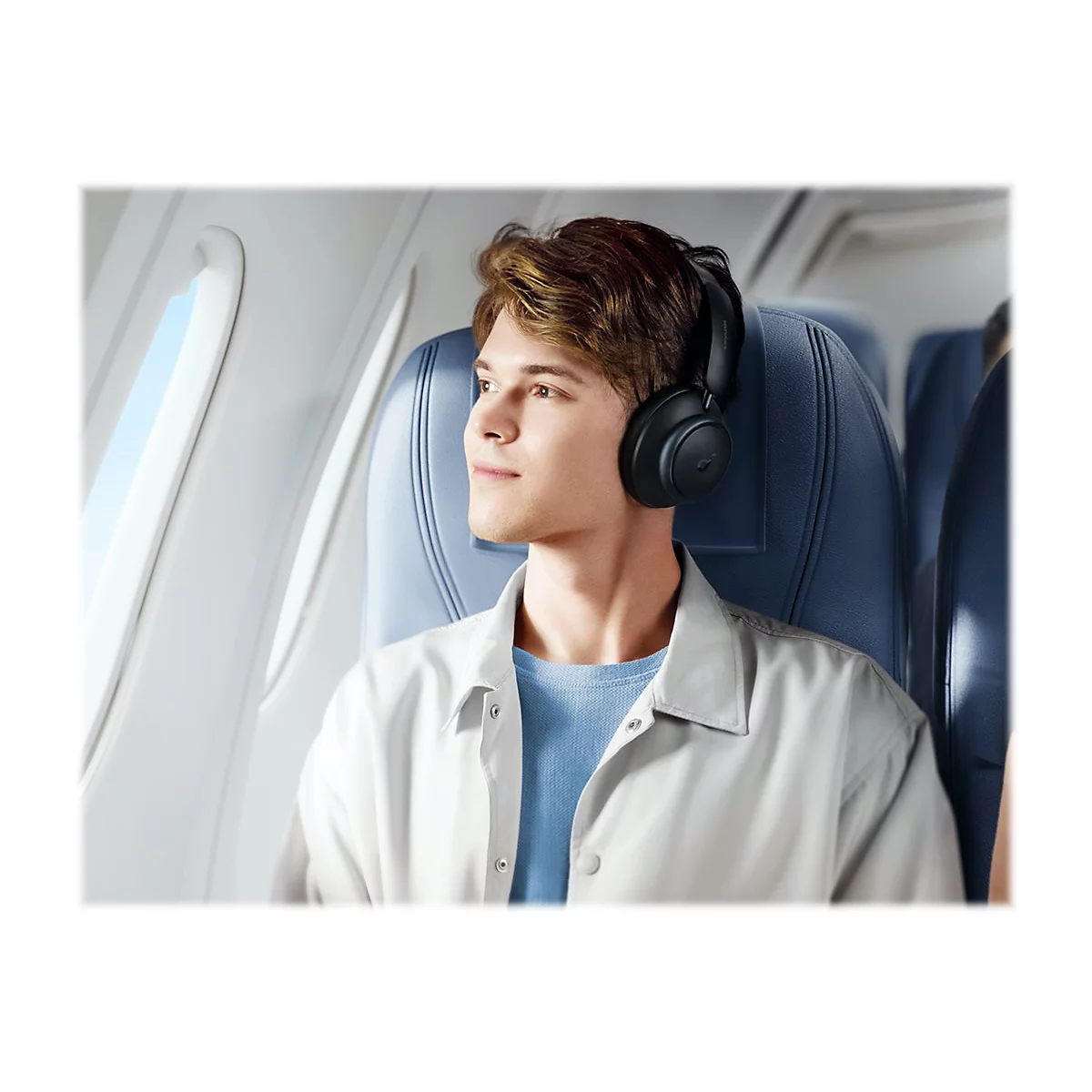 Ein junger Mann im Flugzeug mit KopfhÃ¶rern. Er schaut aus dem Fenster und scheint entspannt.