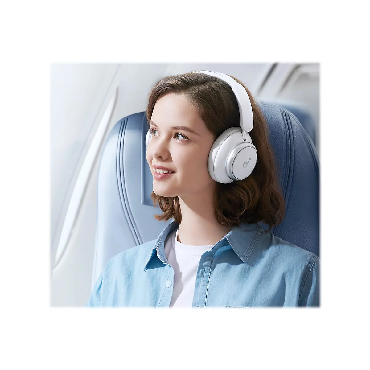 Junge Frau im Flugzeug mit weiÃŸen KopfhÃ¶rern, lÃ¤chelnd.