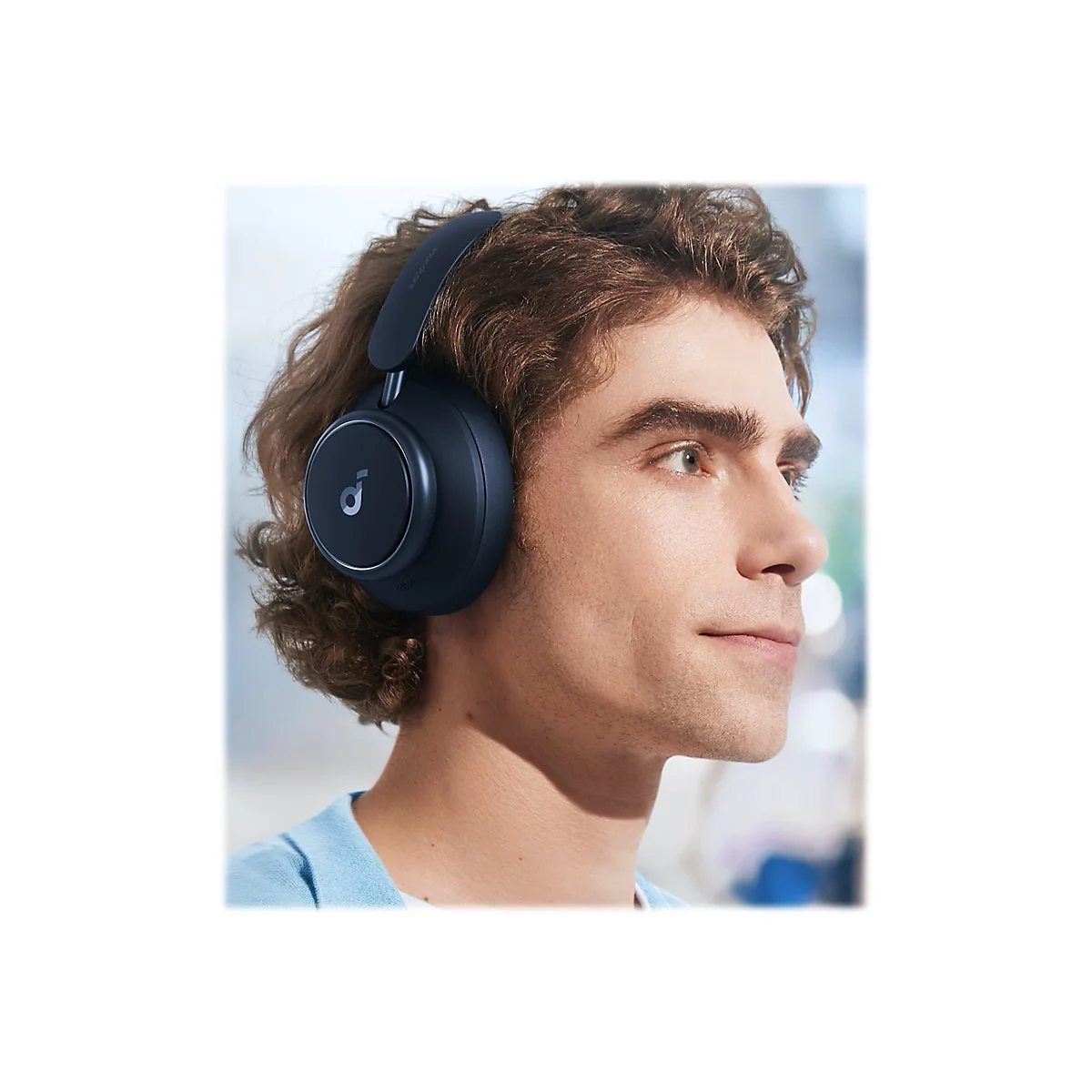 Ein junger Mann trÃ¤gt blaue Over-Ear-KopfhÃ¶rer. Er blickt nach rechts, im Hintergrund ist eine unscharfe Umgebung.