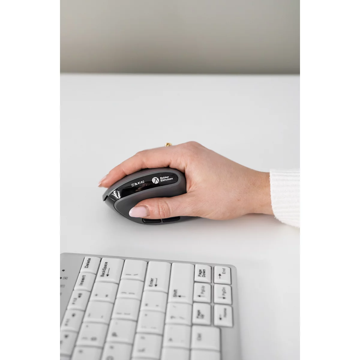 Souris grise dans la main. Clavier à côté. La souris indique "Bluetooth".