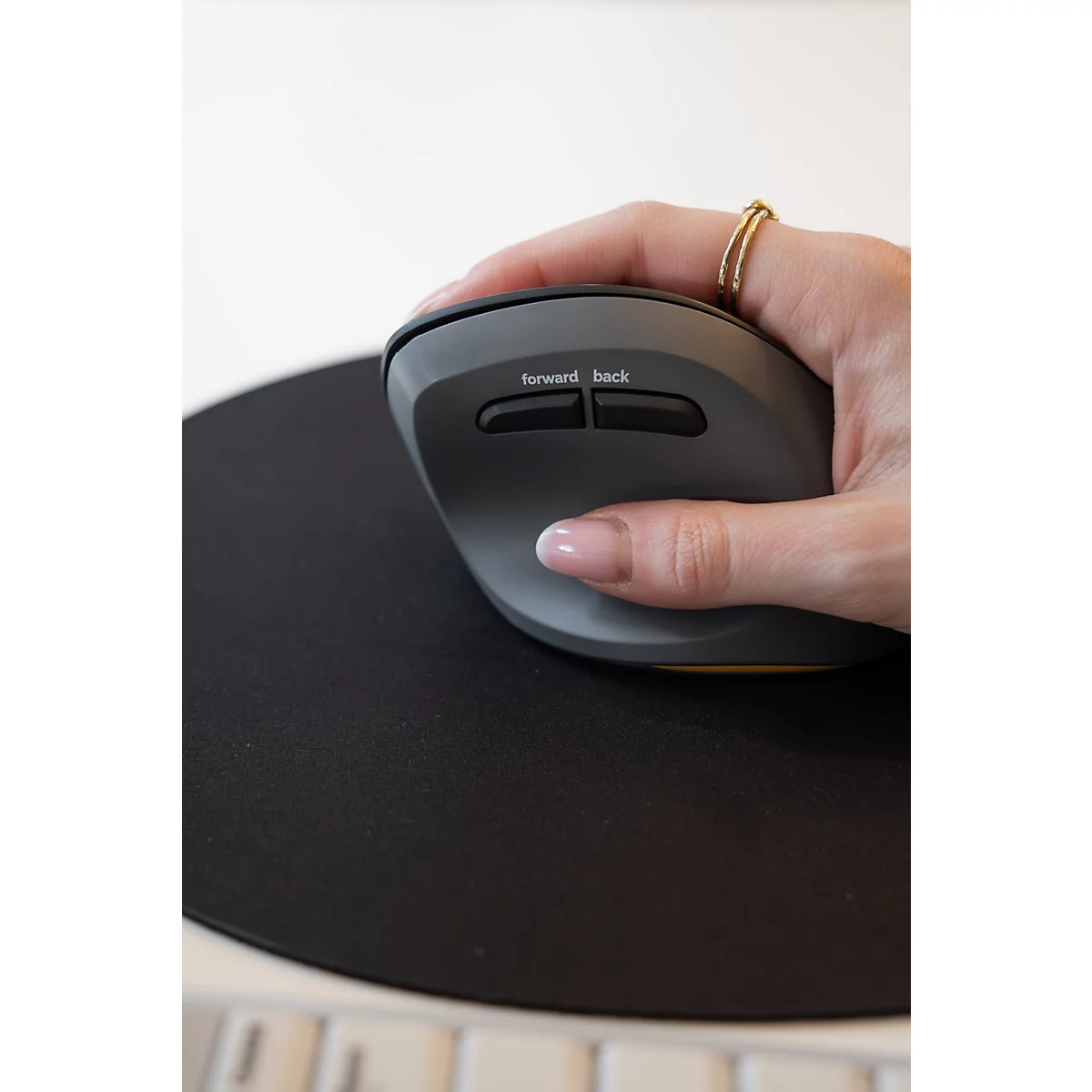 Une main utilise une souris ergonomique grise avec les inscriptions 'forward' et 'back' sur un tapis de souris noir.