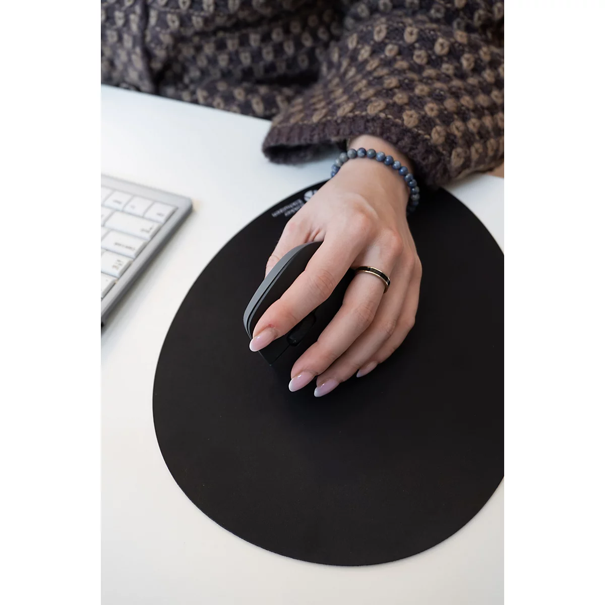 Main manipulant une souris d'ordinateur noire sur un tapis de souris rond et noir.