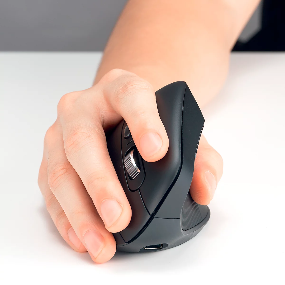 Gros plan d'une main tenant une souris noire verticale. La molette de défilement et les boutons sont visibles.