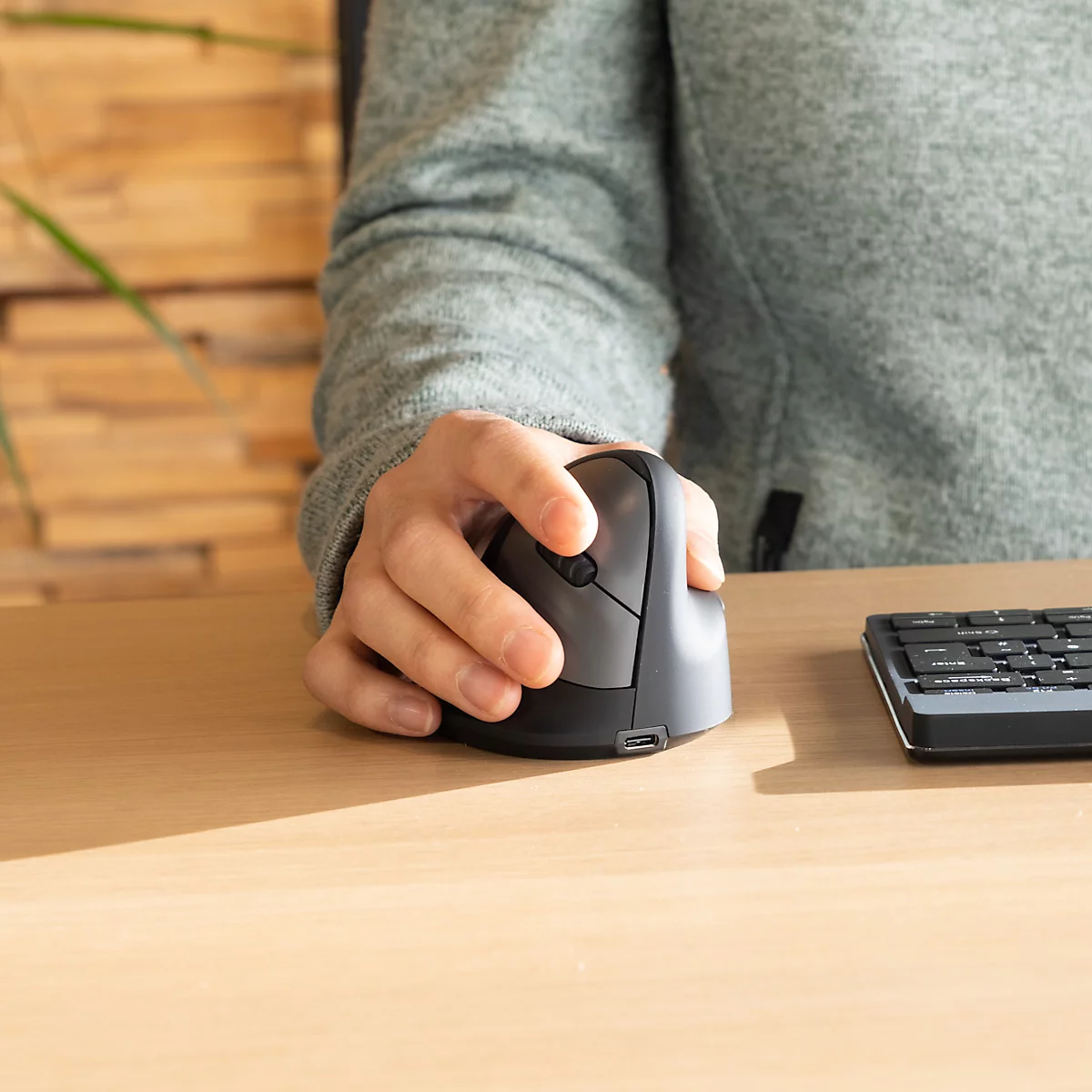 Gros plan d'une personne utilisant une souris ergonomique sur un bureau. À côté, un clavier.
