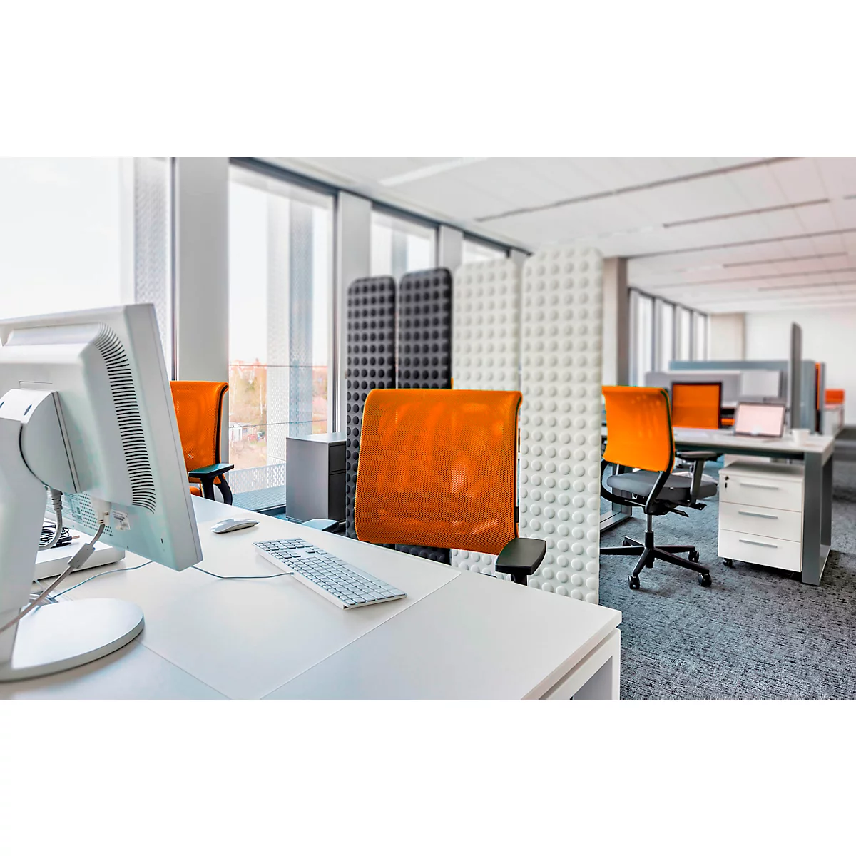 Bureau avec bureaux blancs, ordinateurs, chaises orange et séparateurs.