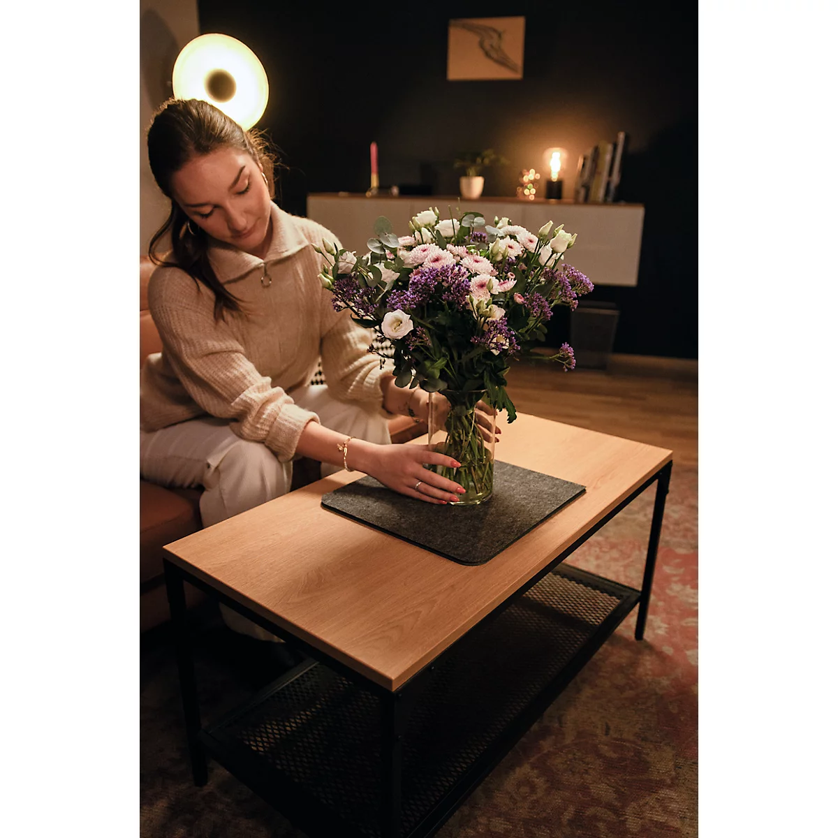 Jeune femme arrangeant un bouquet de fleurs dans un vase sur une table basse.