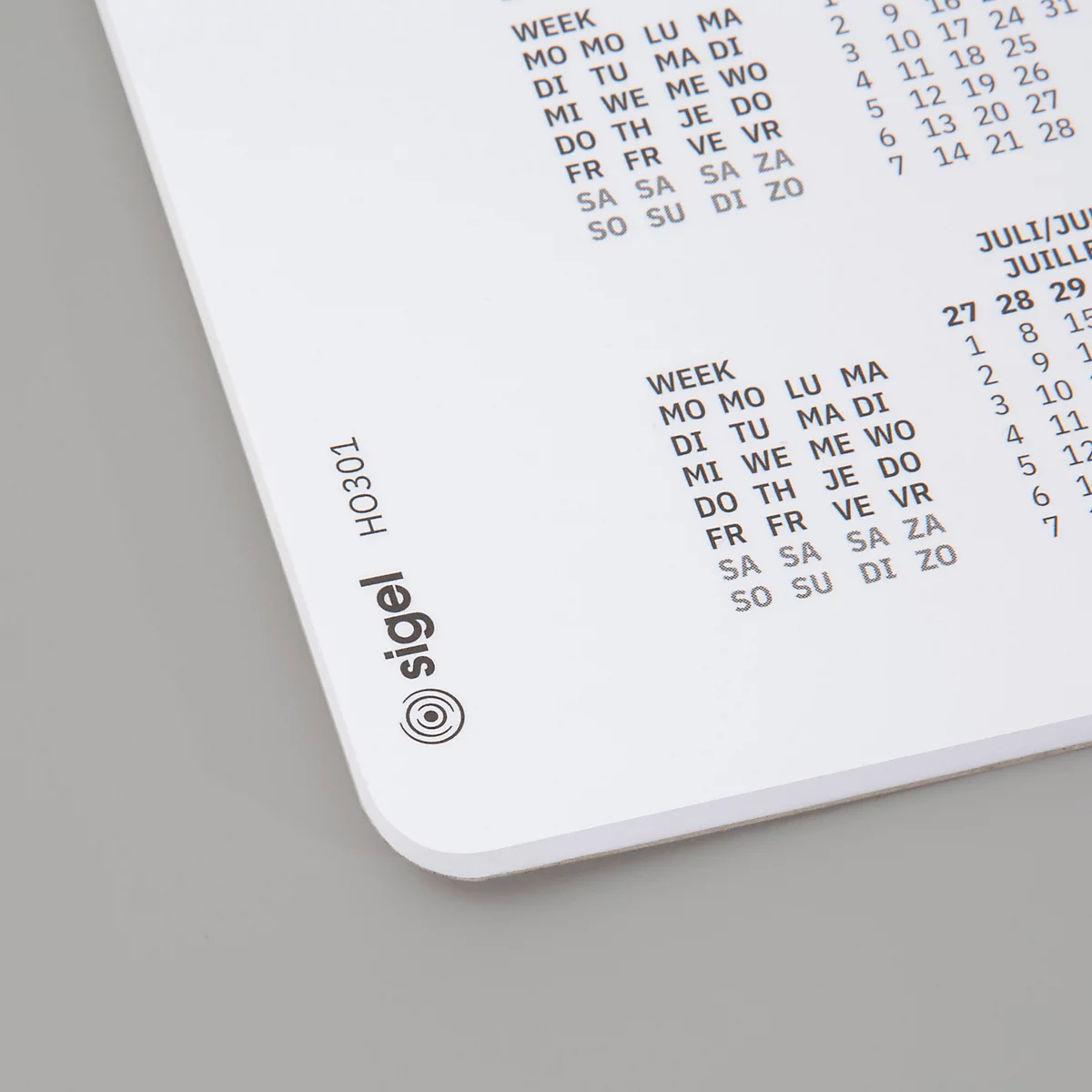 Gros plan d'un calendrier blanc avec un fond gris. Le logo Sigel et un calendrier hebdomadaire sont visibles.