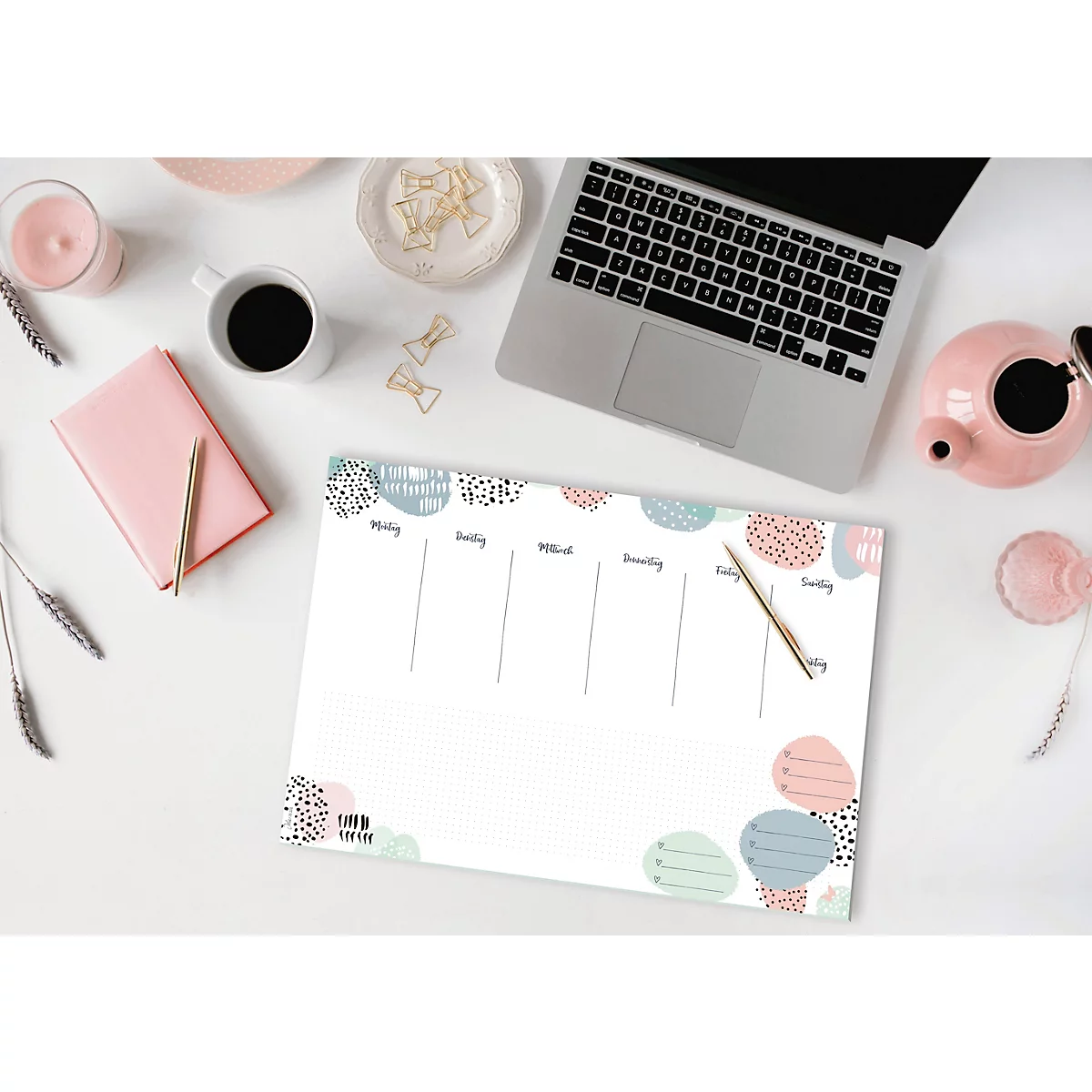 Un bureau avec un planificateur hebdomadaire, un ordinateur portable, un stylo, une tasse, un carnet, une bougie et une théière.