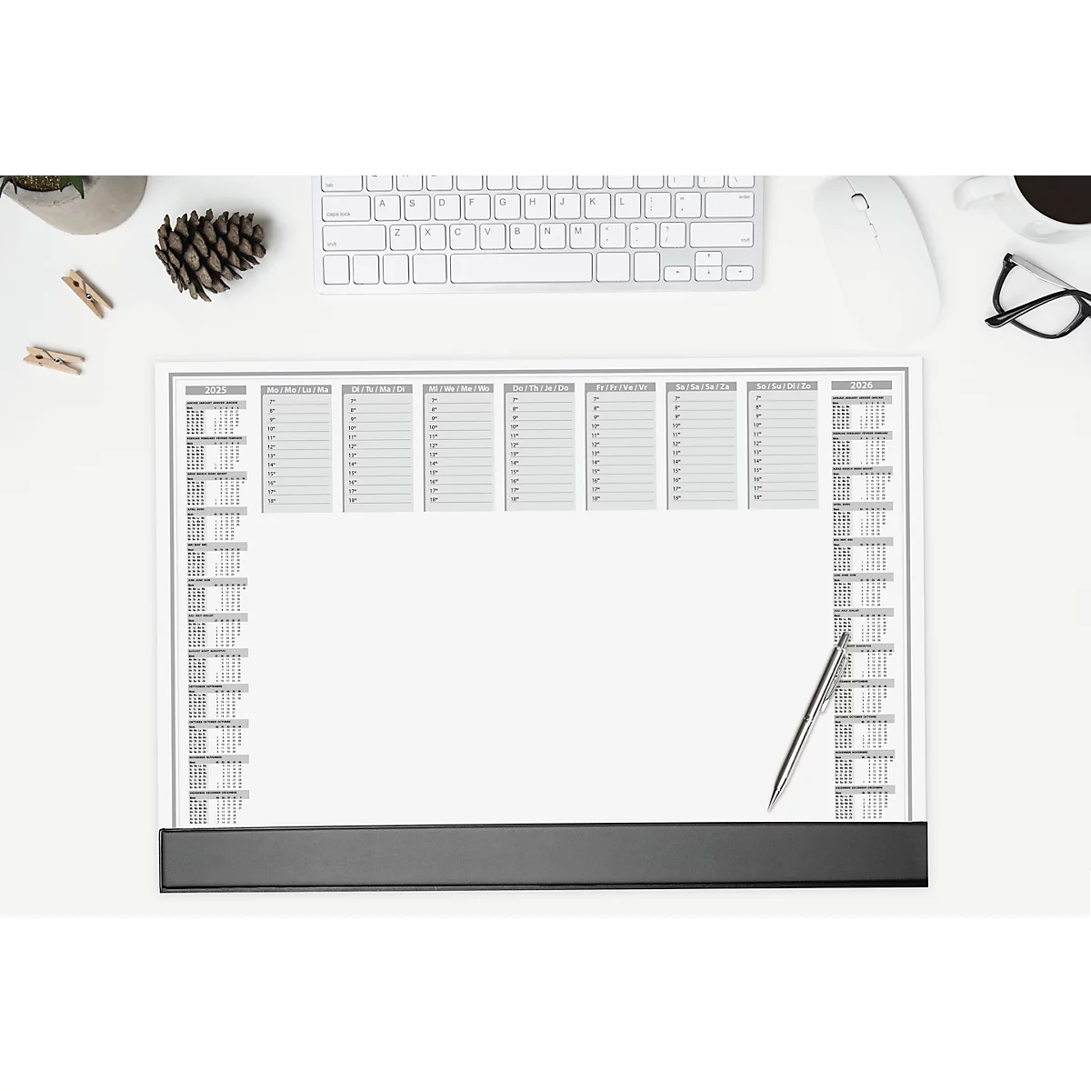Vue de dessus d'un bureau. Un bloc calendrier avec des champs gris et un stylo argenté est posé sur la table. A côté : clavier, souris, lunettes.