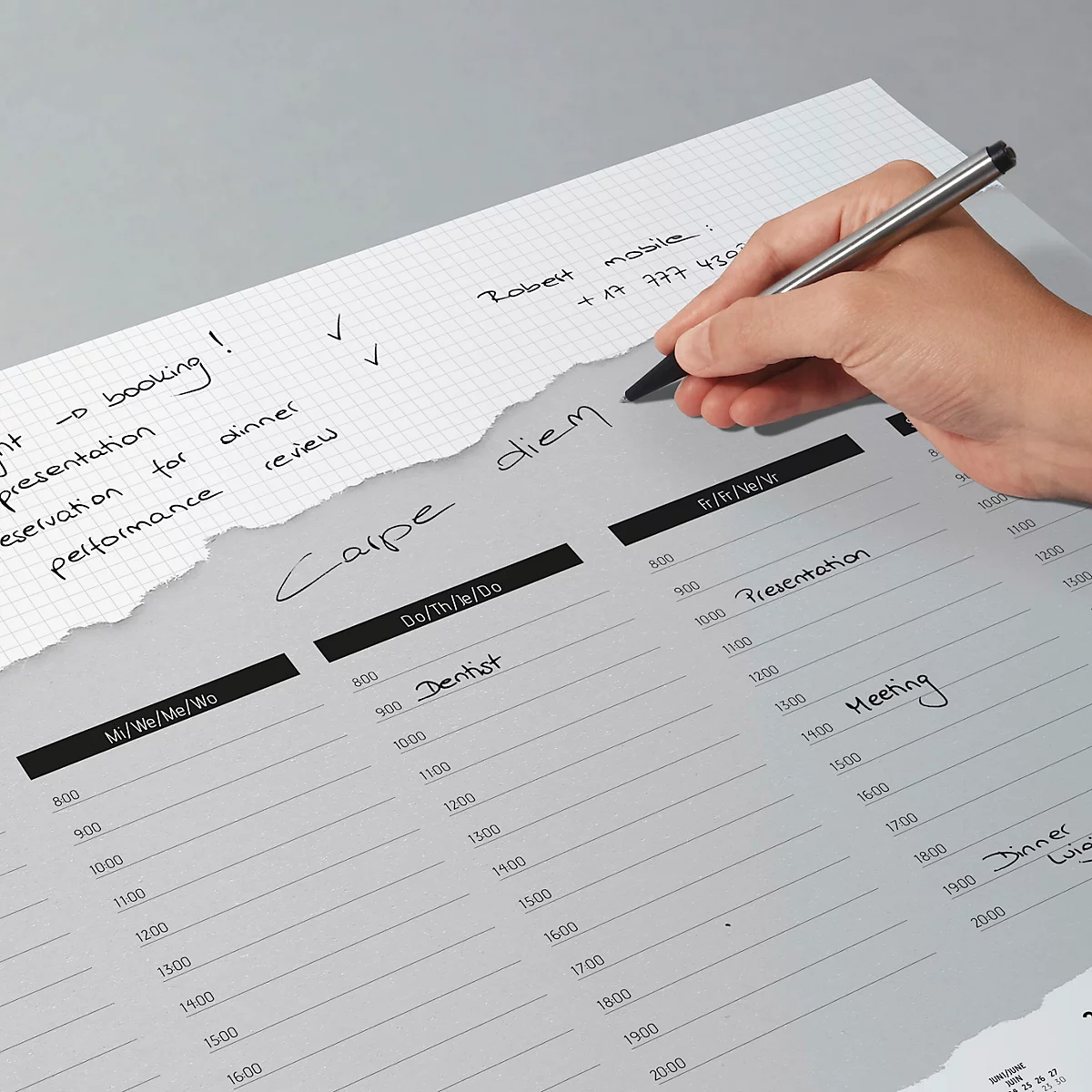 Une personne écrit avec un stylo dans un agenda. L'agenda montre les semaines et les heures quotidiennes. Le bord supérieur est déchiré et porte des notes.