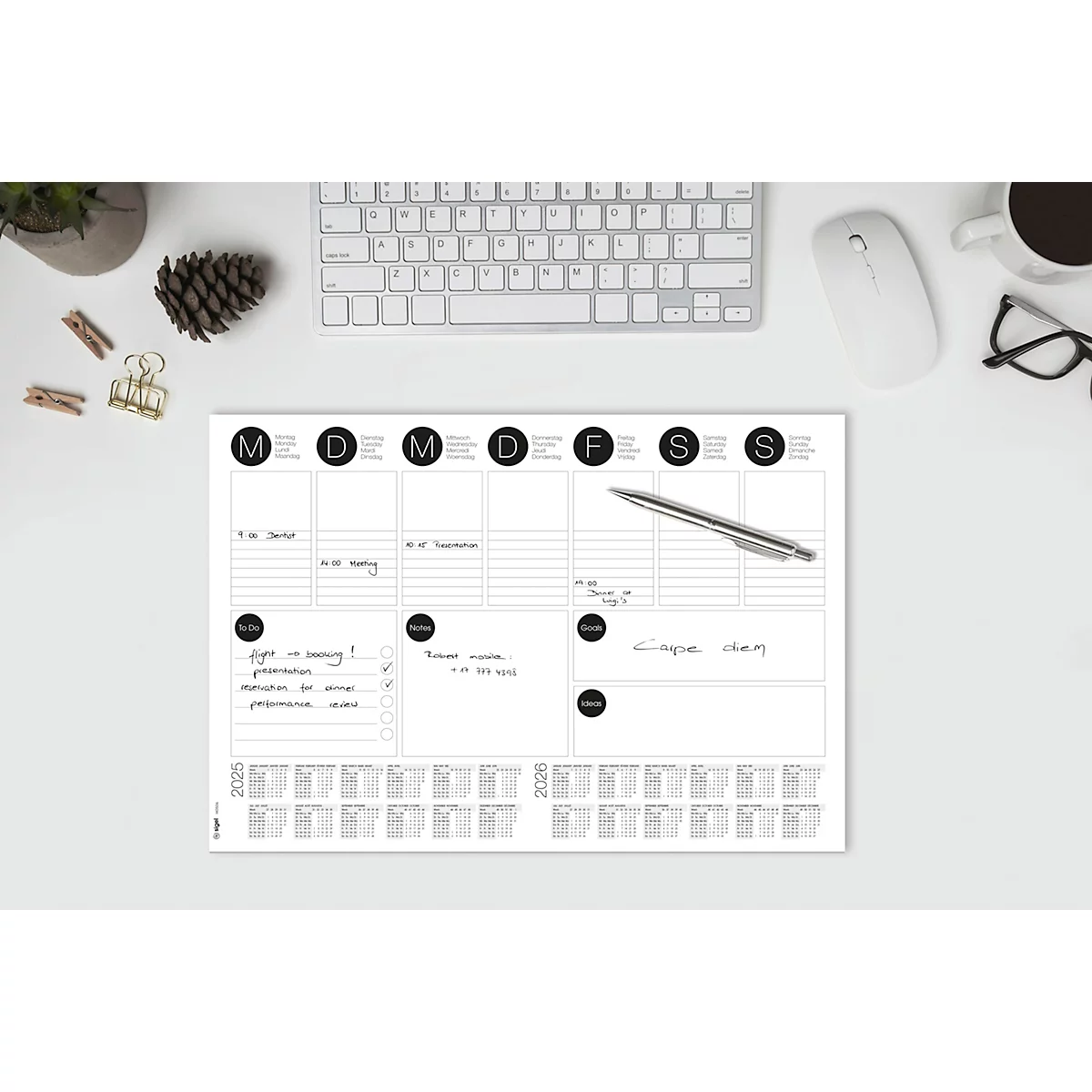 Planificateur hebdomadaire avec des notes manuscrites sur un bureau avec clavier, souris, lunettes et tasse à café. Comprend un stylo à bille.