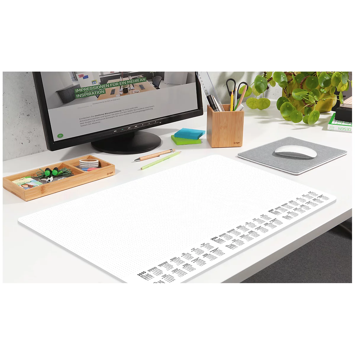 Tapis de bureau blanc avec bande de calendrier et fournitures de bureau : moniteur, stylos, souris, plantes.