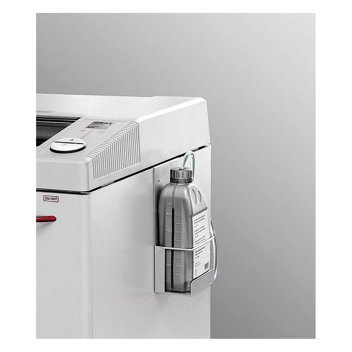 Close-up of a white paper shredder with an attached gray oil bottle in a holder. The bottle has a cap with a hanging loop.