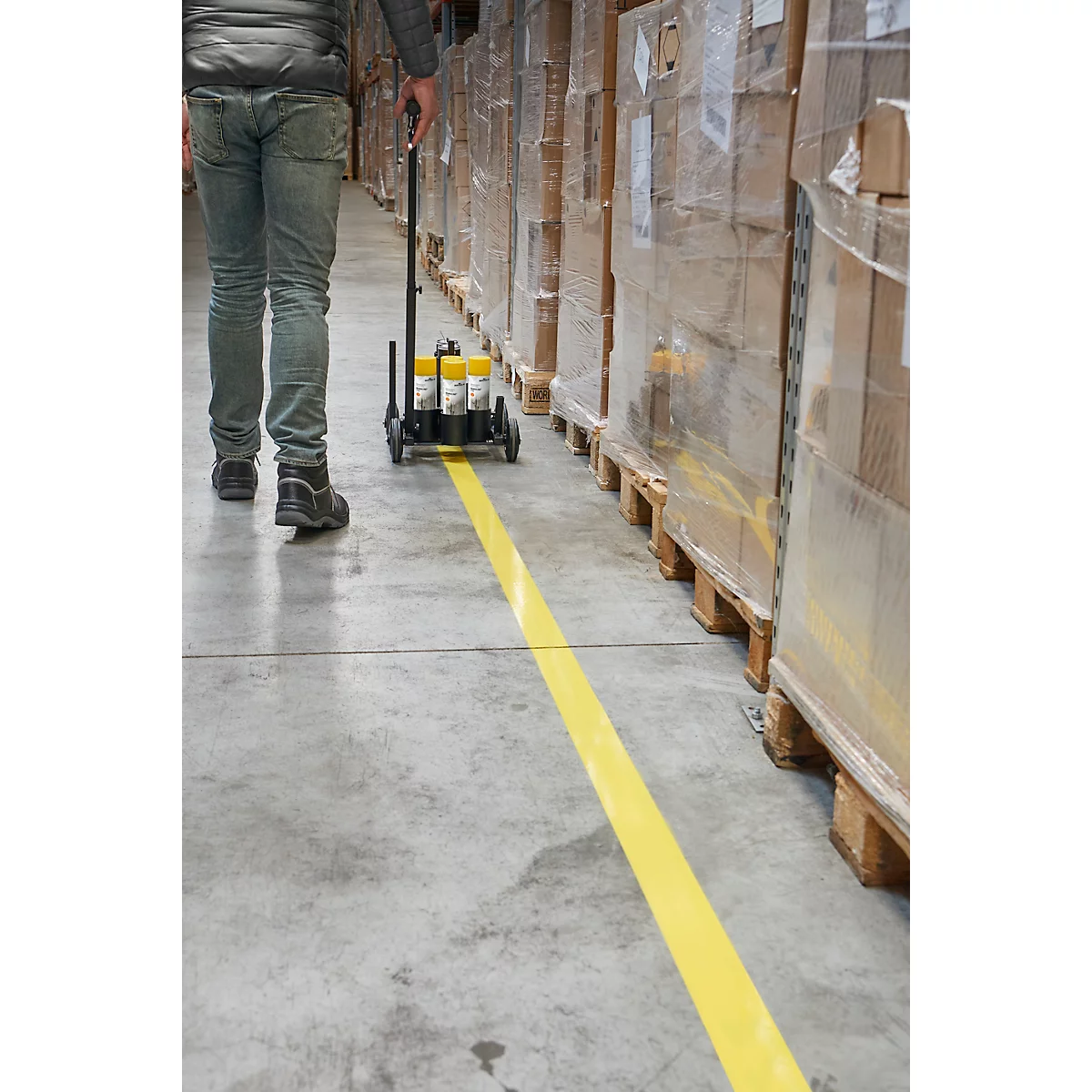 Personne avec une machine de marquage au sol jaune dans un entrepôt. Ligne jaune sur un sol en béton. Palettes avec des boîtes emballées.