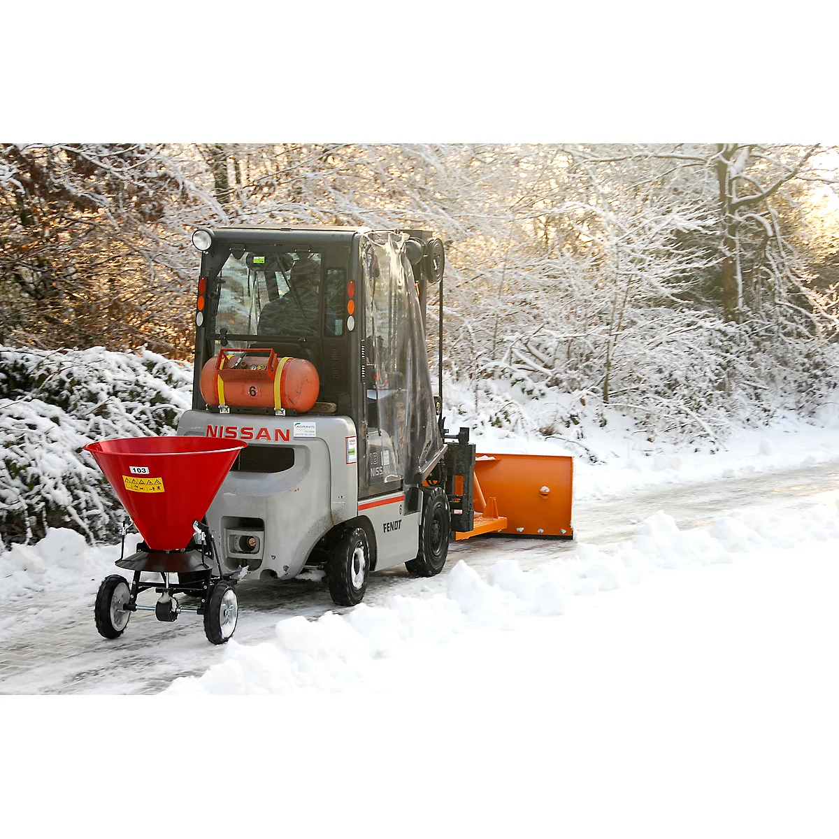 Gray Nissan snowplow with red salt spreader and orange plow on a snow-covered road.