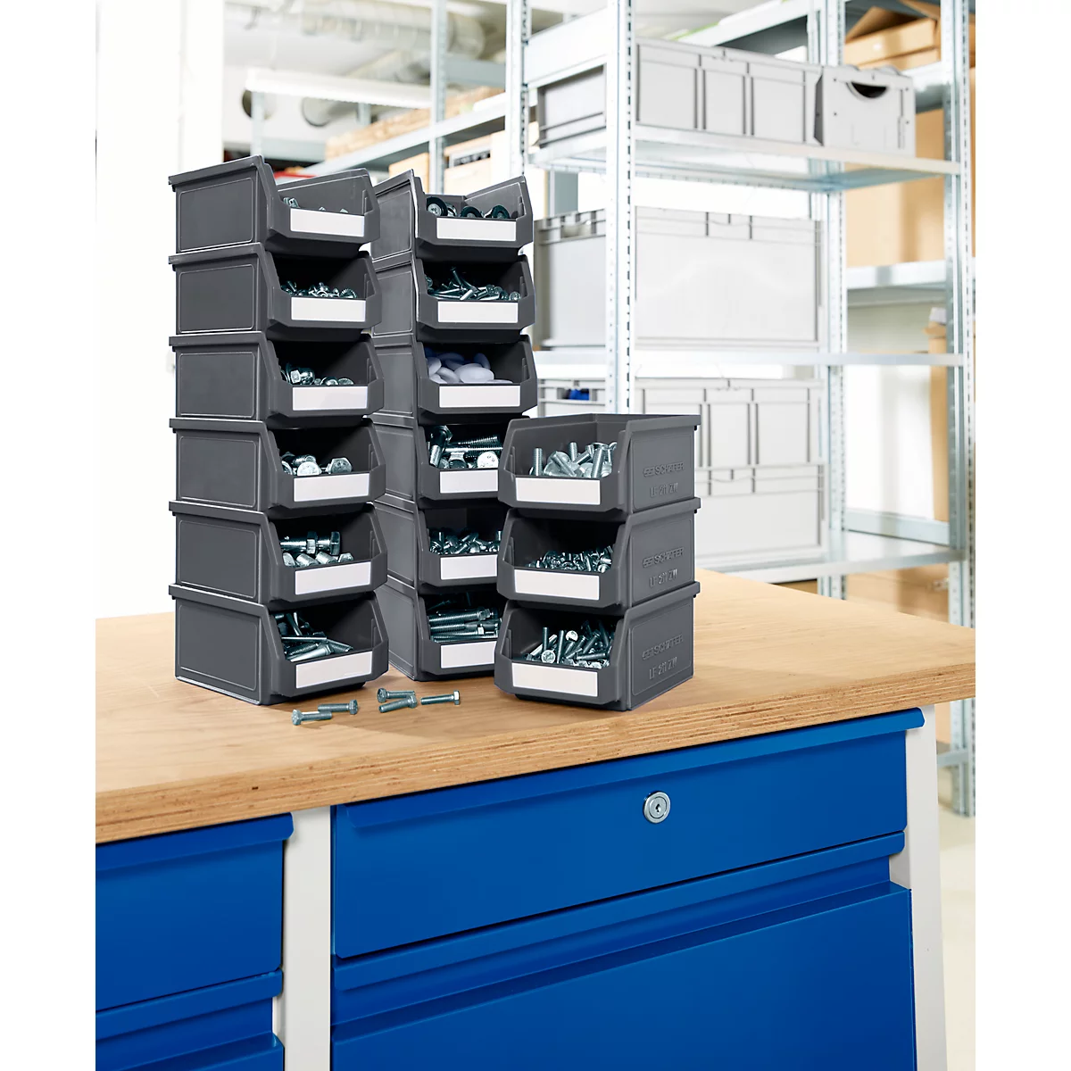 Boîtes de rangement grises avec vis sur un établi. Des étagères sont visibles en arrière-plan.