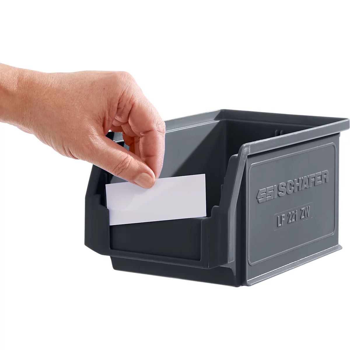 Boîte en plastique grise dans laquelle une main insère une étiquette blanche. La boîte indique "SCHÄFER" et "LF 221 ZV".
