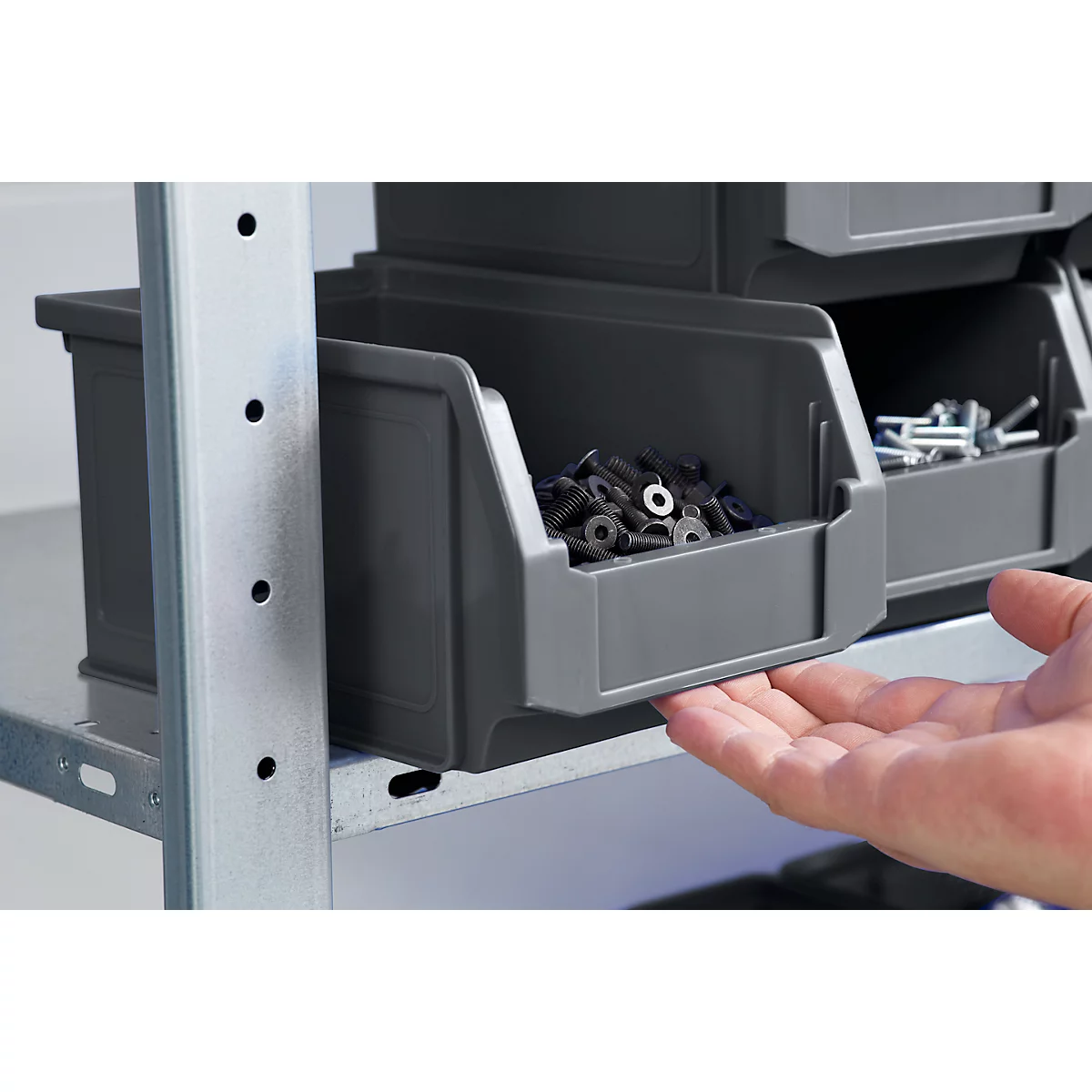 Tiroirs gris remplis de vis sur une étagère métallique, une main ouvre le tiroir.