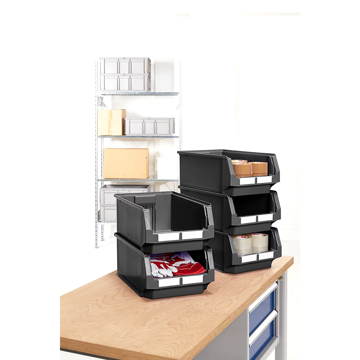 Boîtes de rangement noires sur une table en bois. En arrière-plan, une étagère avec des boîtes.