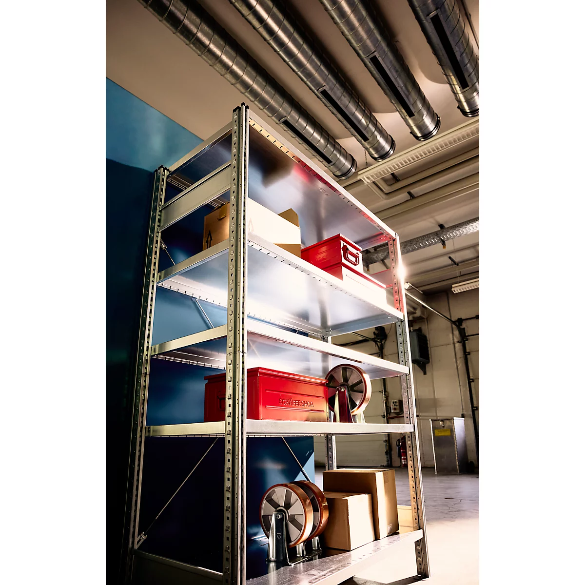 Metallregal mit roten Werkzeugboxen und Rollen in einem Lagerraum mit Rohren an der Decke.