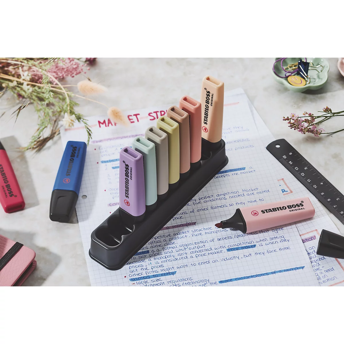 Mehrfarbige Textmarker in Halterung und auf Notizen. Rechts liegt ein rosa Textmarker.