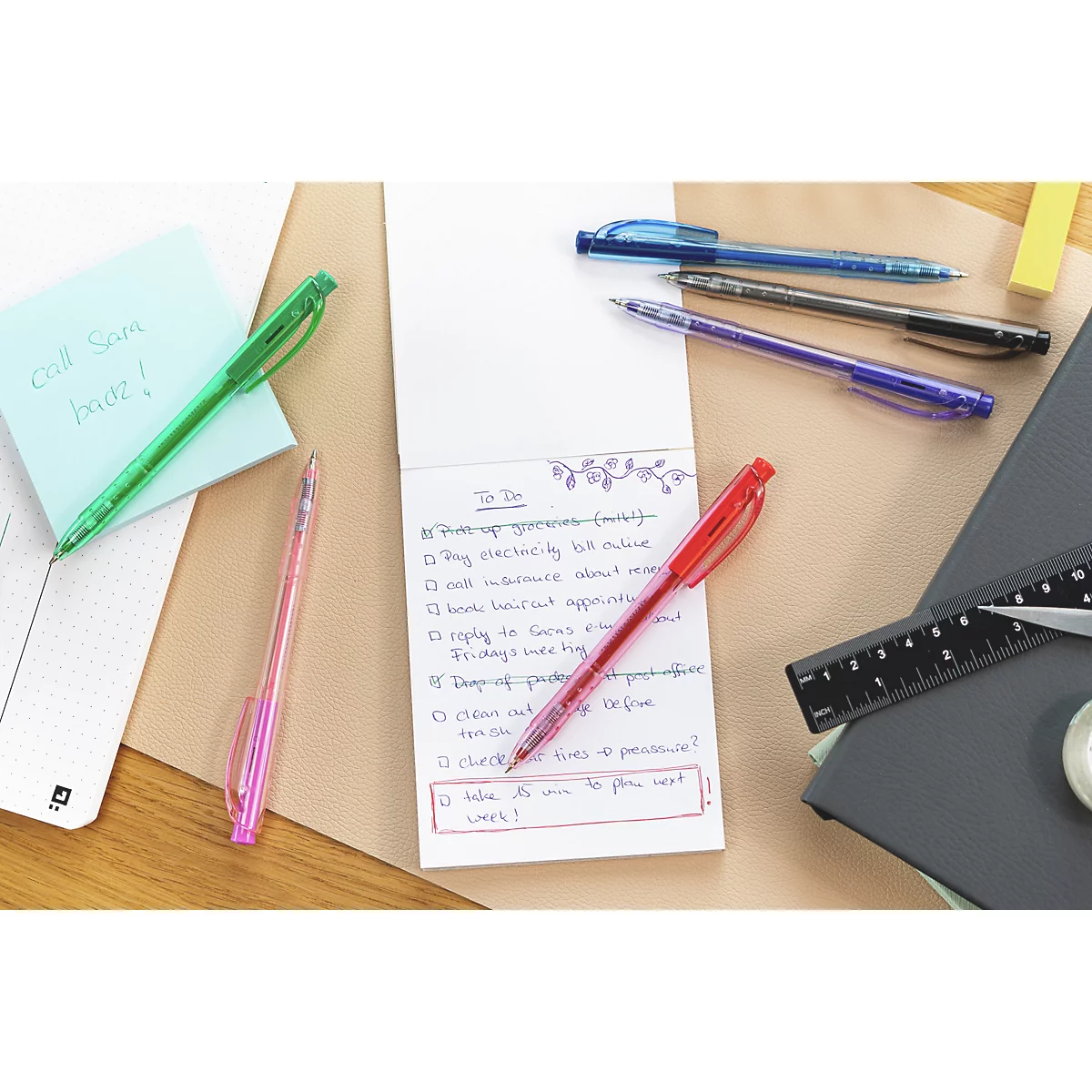 Nahaufnahme von Stiften und Notizen auf einem Tisch. Ein roter Stift liegt auf einem Notizblock mit einer To-Do-Liste.