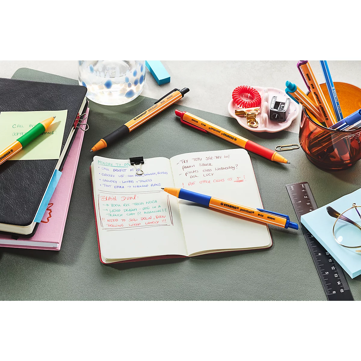 Uitzicht op een bureau met notitieboekjes, pennen en notities. Een open notitieboek met handgeschreven notities staat centraal.