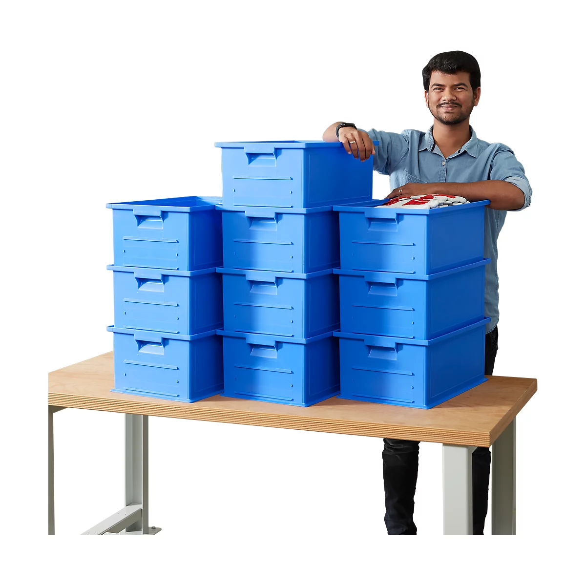 A man stands next to stacked, blue boxes on a table. Some boxes contain clothes.
